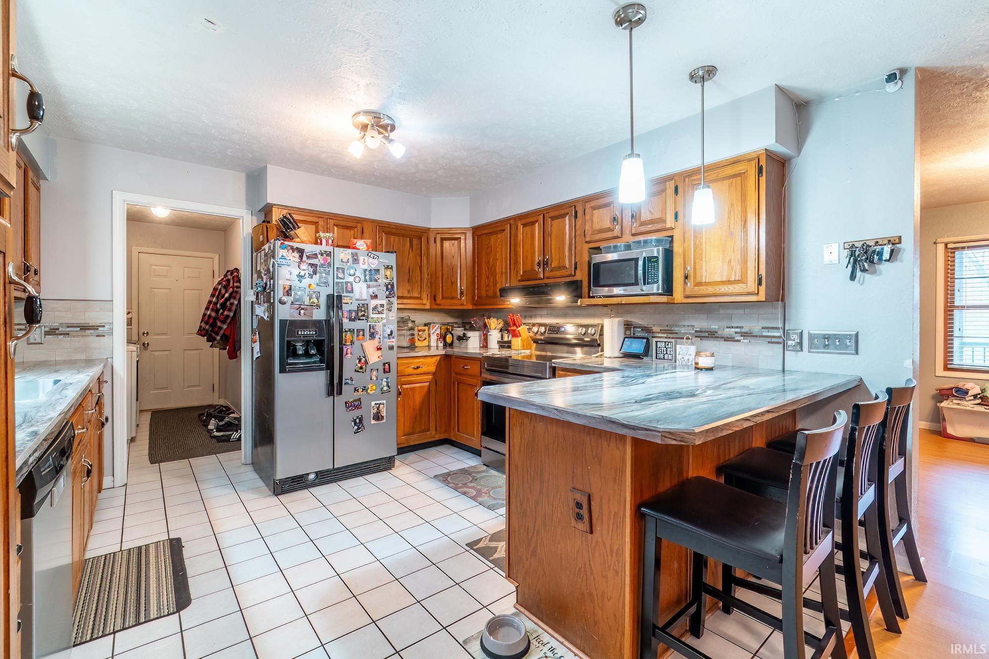 Kitchen featuring wood finish cabinets, tasteful backsplash, stainless steel appliances, a peninsula, and a textured ceiling