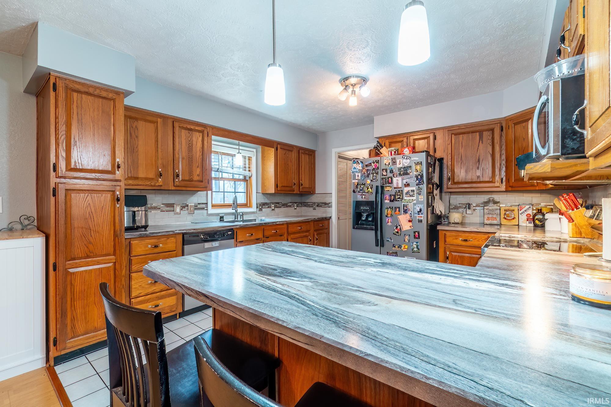Kitchen featuring wood finish cabinets, stainless steel appliances, light tile patterned flooring, a peninsula, and tasteful backsplash