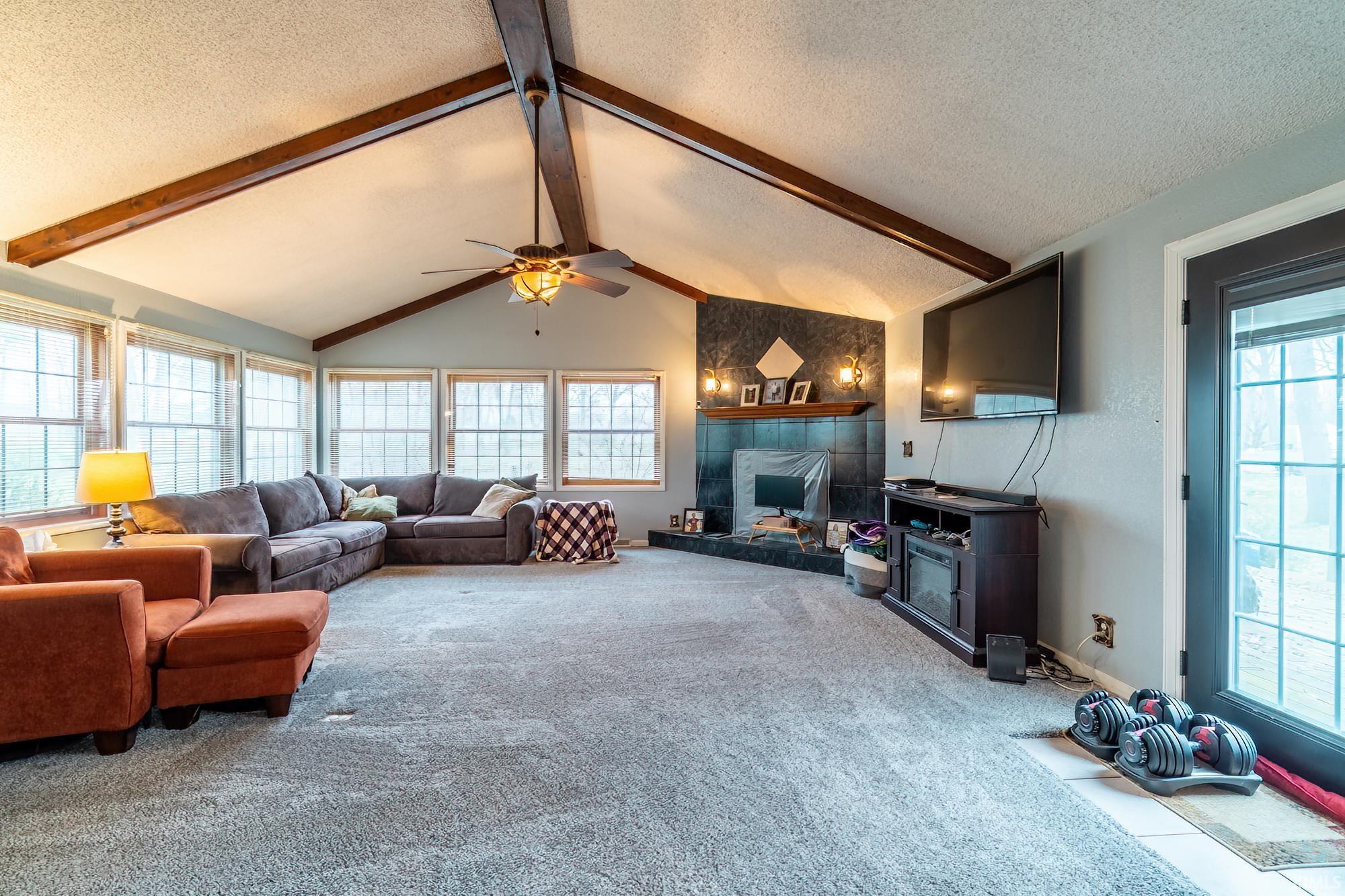Carpeted living room featuring a textured ceiling, ceiling fan, and vaulted ceilings with fireplace overlooking back yard