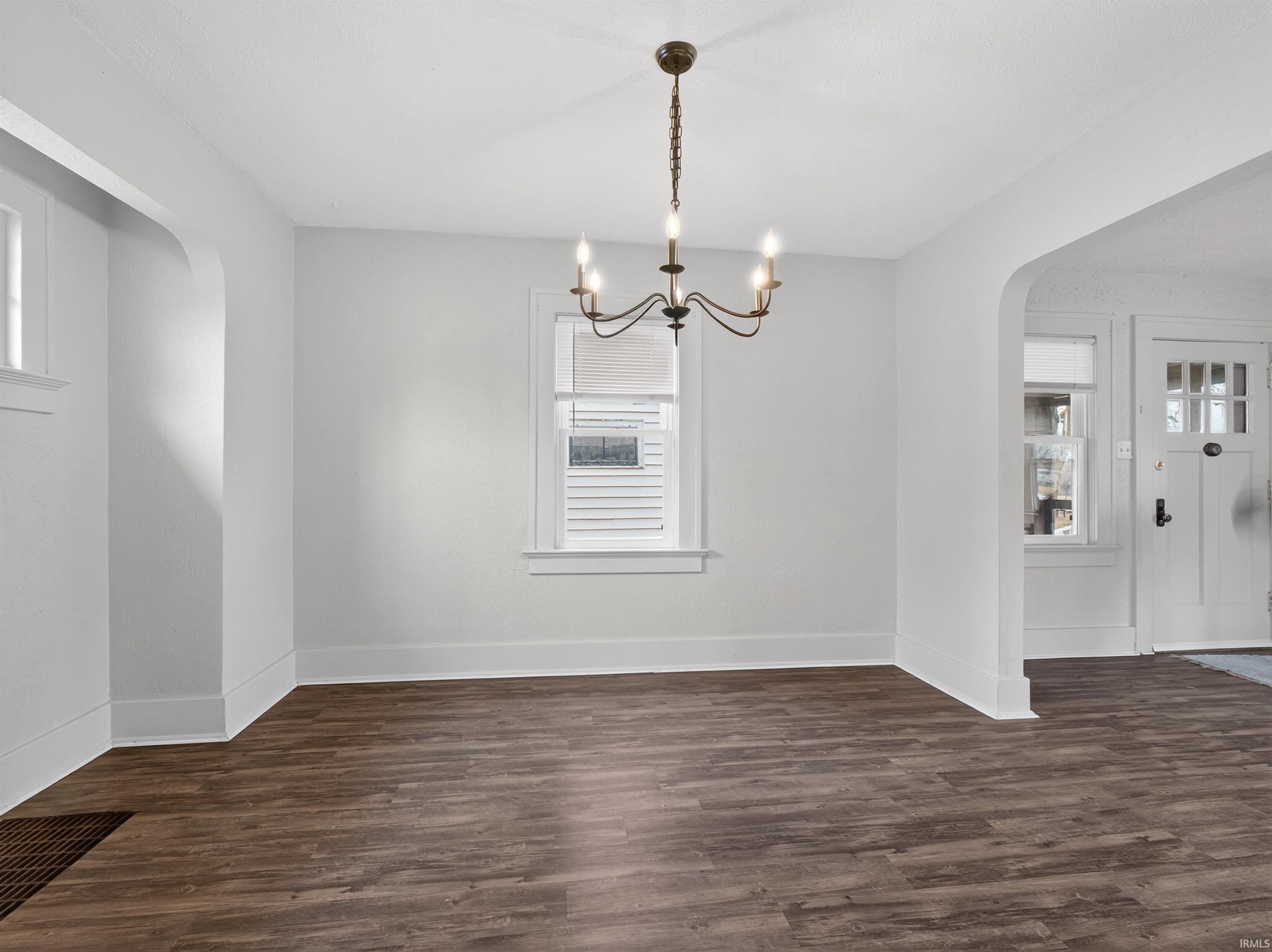 Unfurnished dining area with arched walkways, dark wood finished floors, and hanging lights
