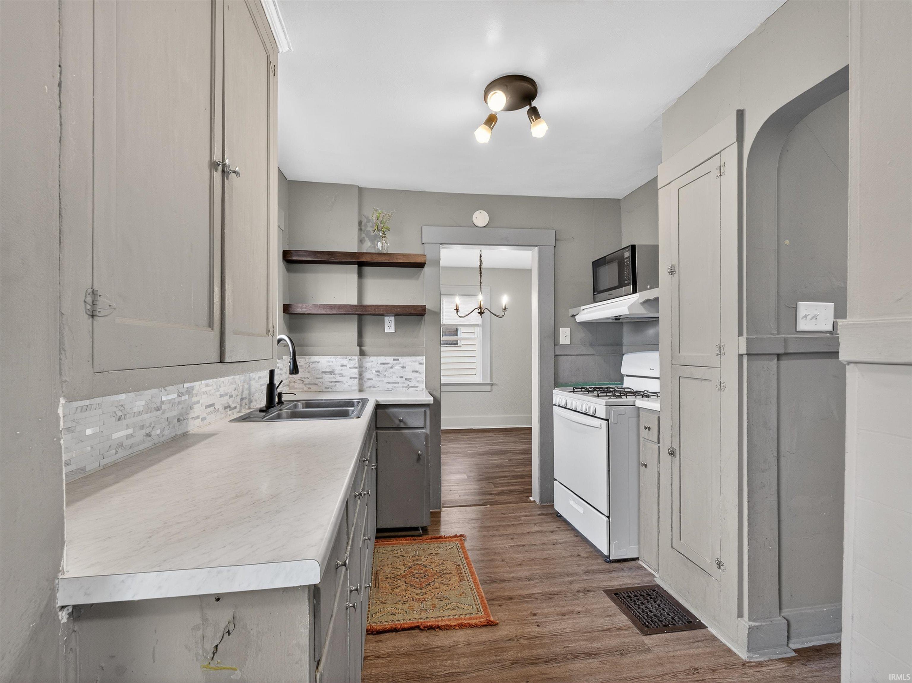 Kitchen with white gas stove, open shelves, gray cabinetry, light wood finished floors, and light countertops