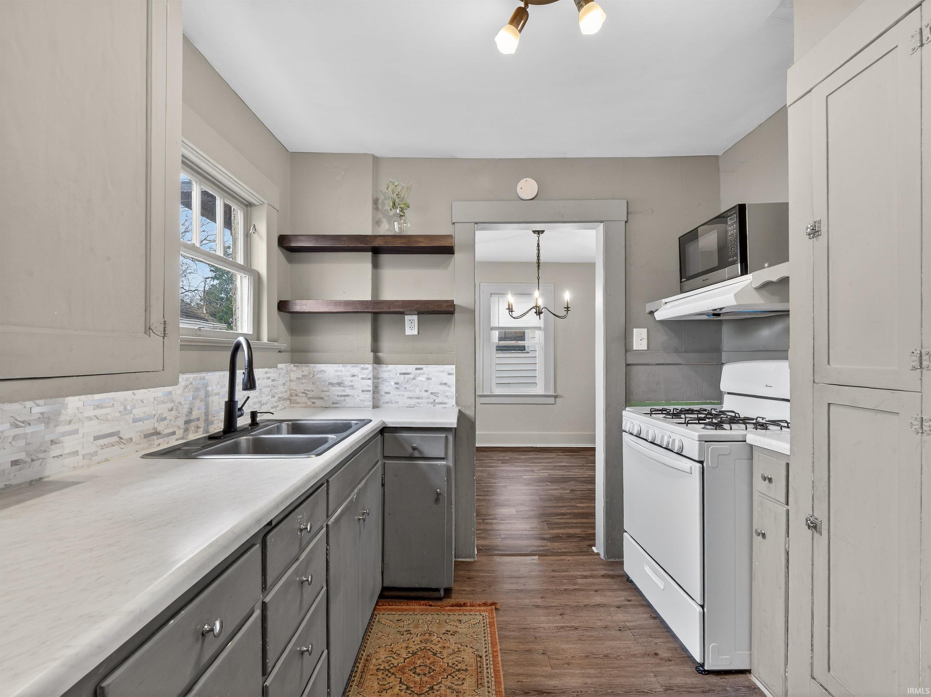 Kitchen featuring open shelves, hanging lights, white range with gas cooktop, light countertops, and plenty of natural light