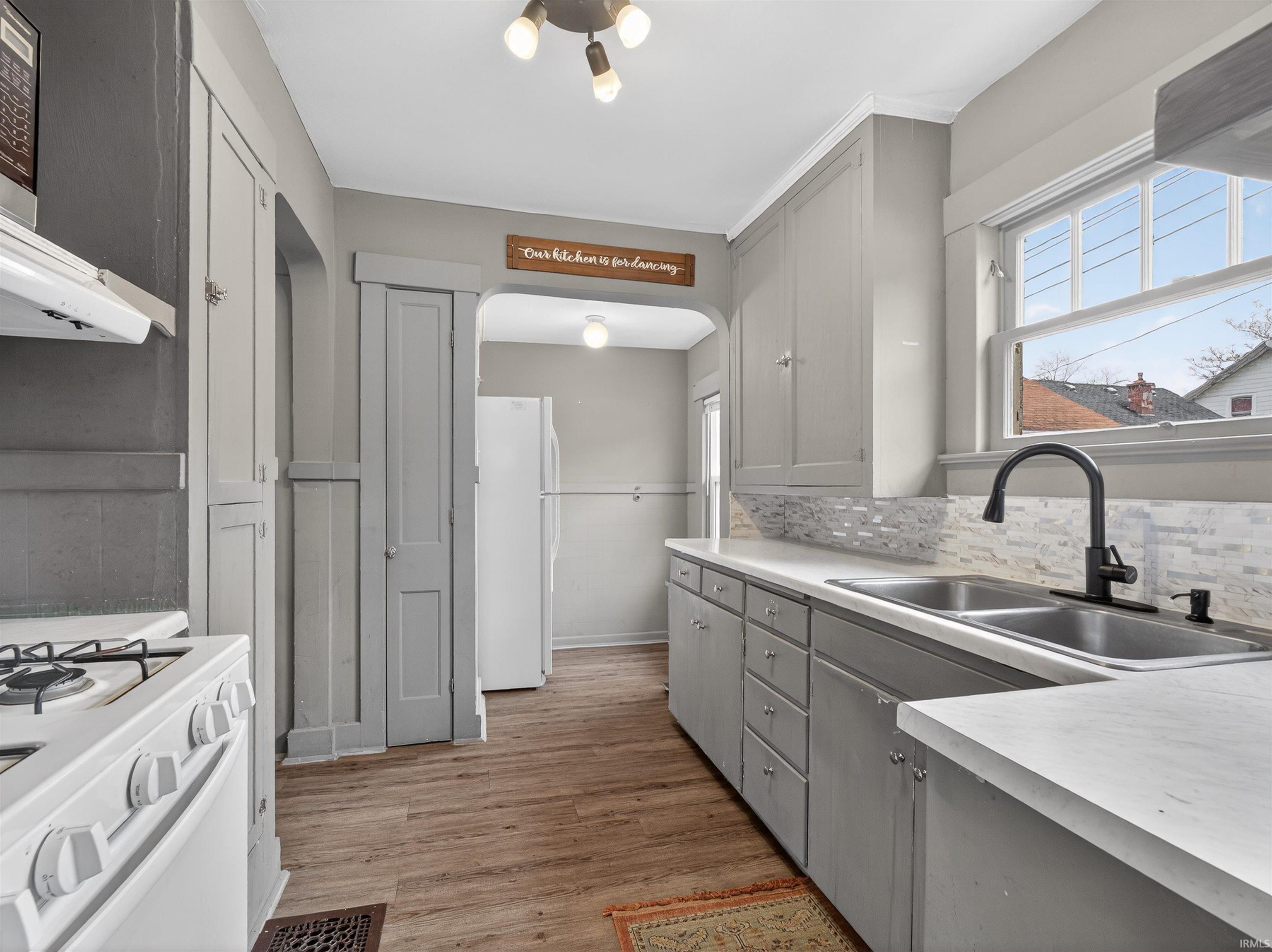Kitchen with gray cabinets, white appliances, light countertops, light wood finished floors, and plenty of natural light