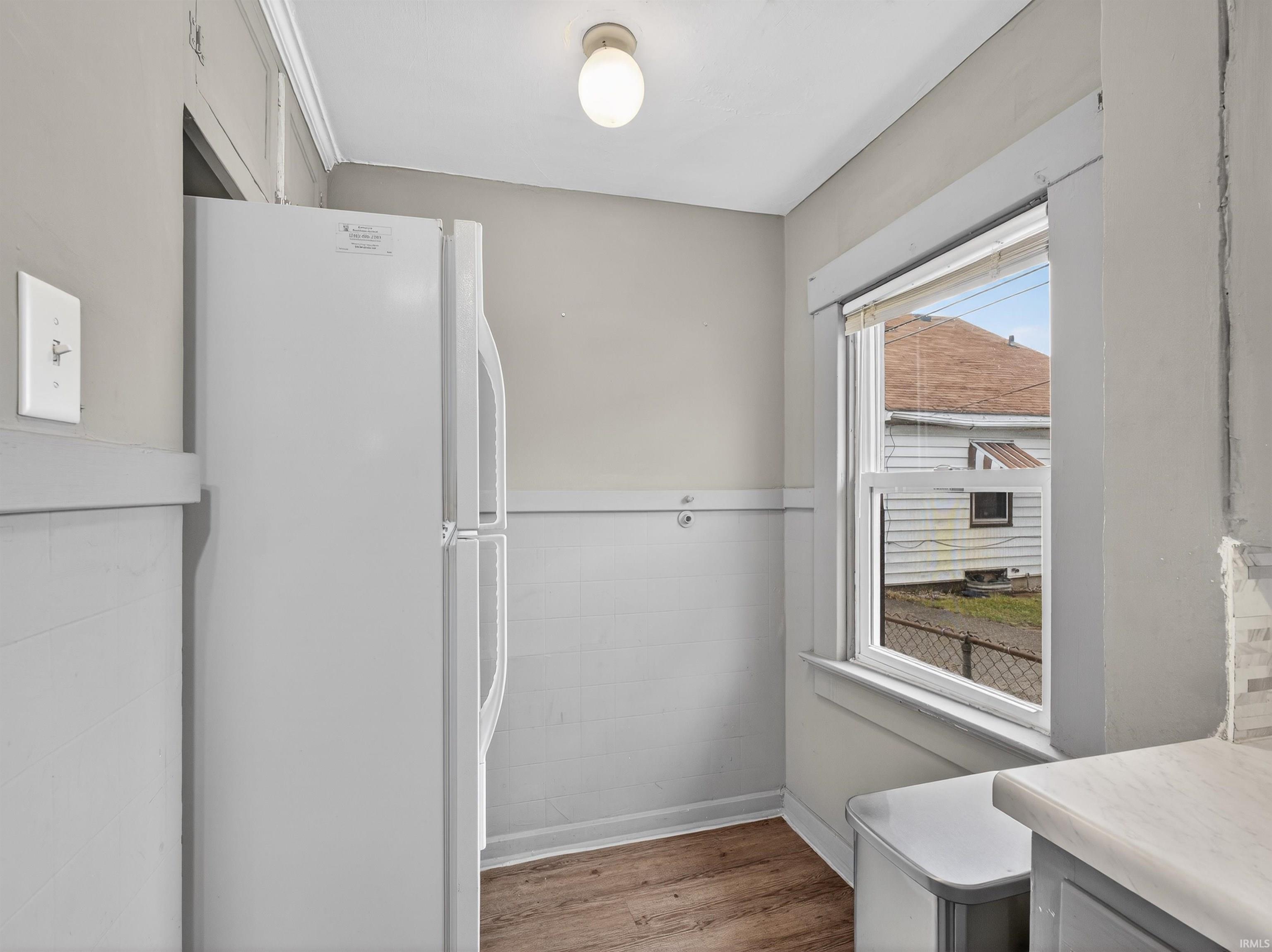 Kitchen featuring freestanding refrigerator, light wood-style floors, tile walls, and a wainscoted wall