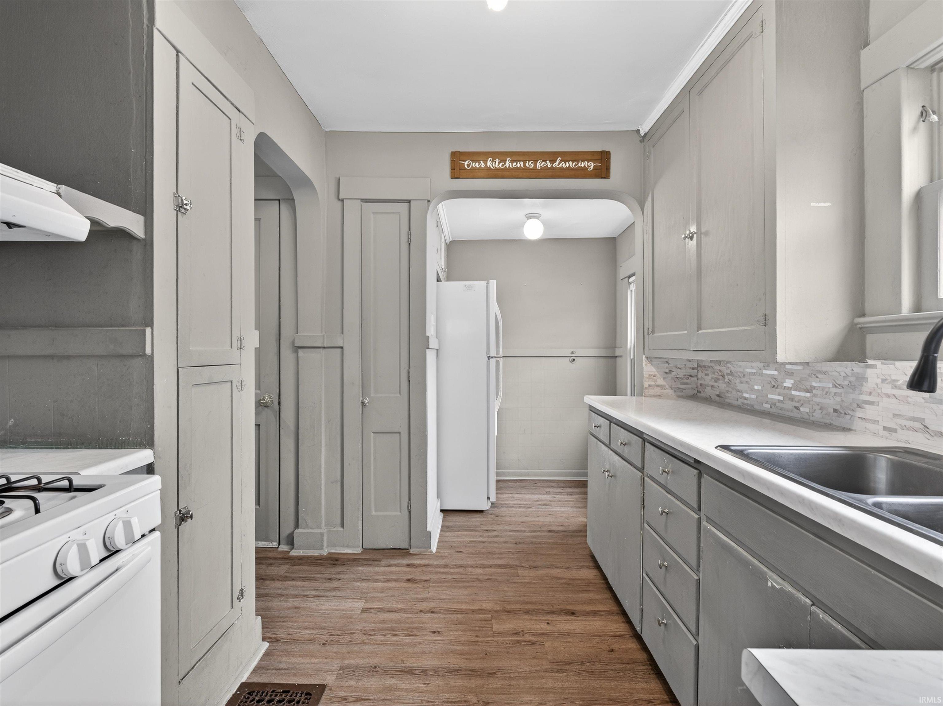 Kitchen featuring light countertops, gray cabinets, white appliances, arched walkways, and light wood-style flooring
