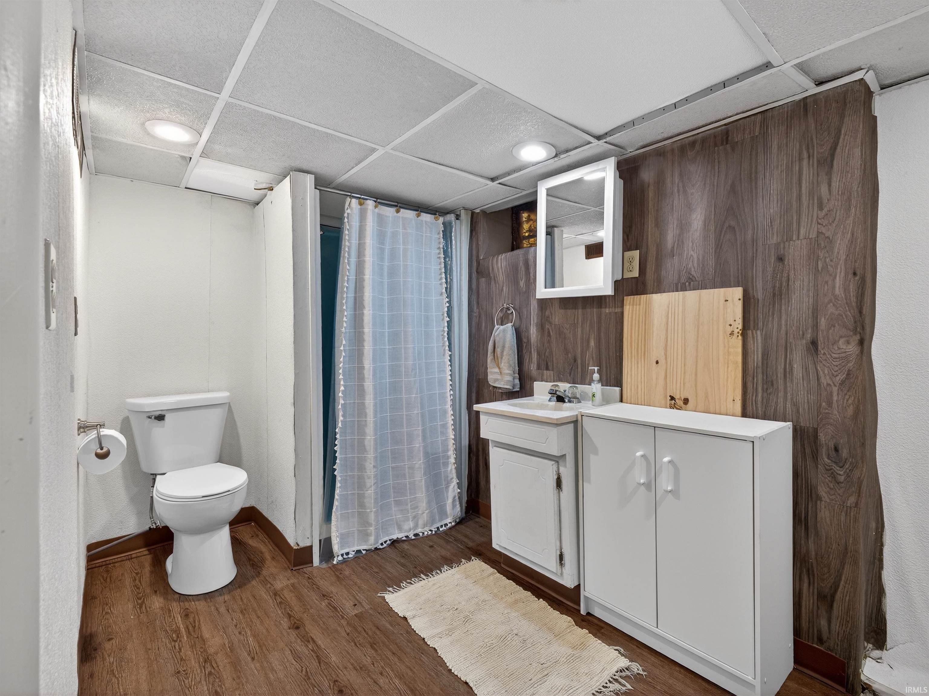 Full bath with vanity, a paneled ceiling, dark wood-type flooring, a shower with shower curtain, and wood walls