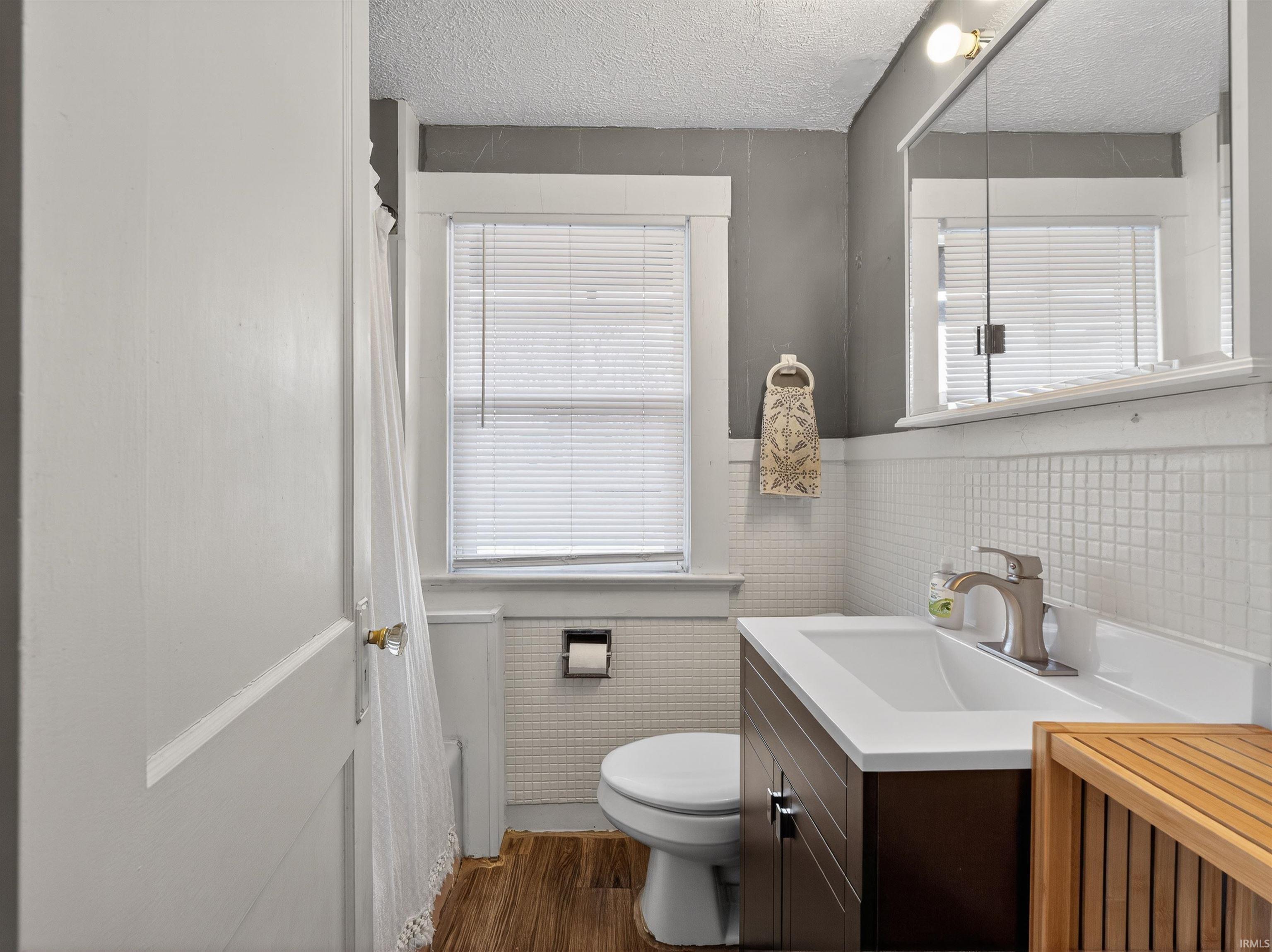 Full bathroom featuring tile walls, vanity, wainscoting, dark wood-style floors, and a textured ceiling