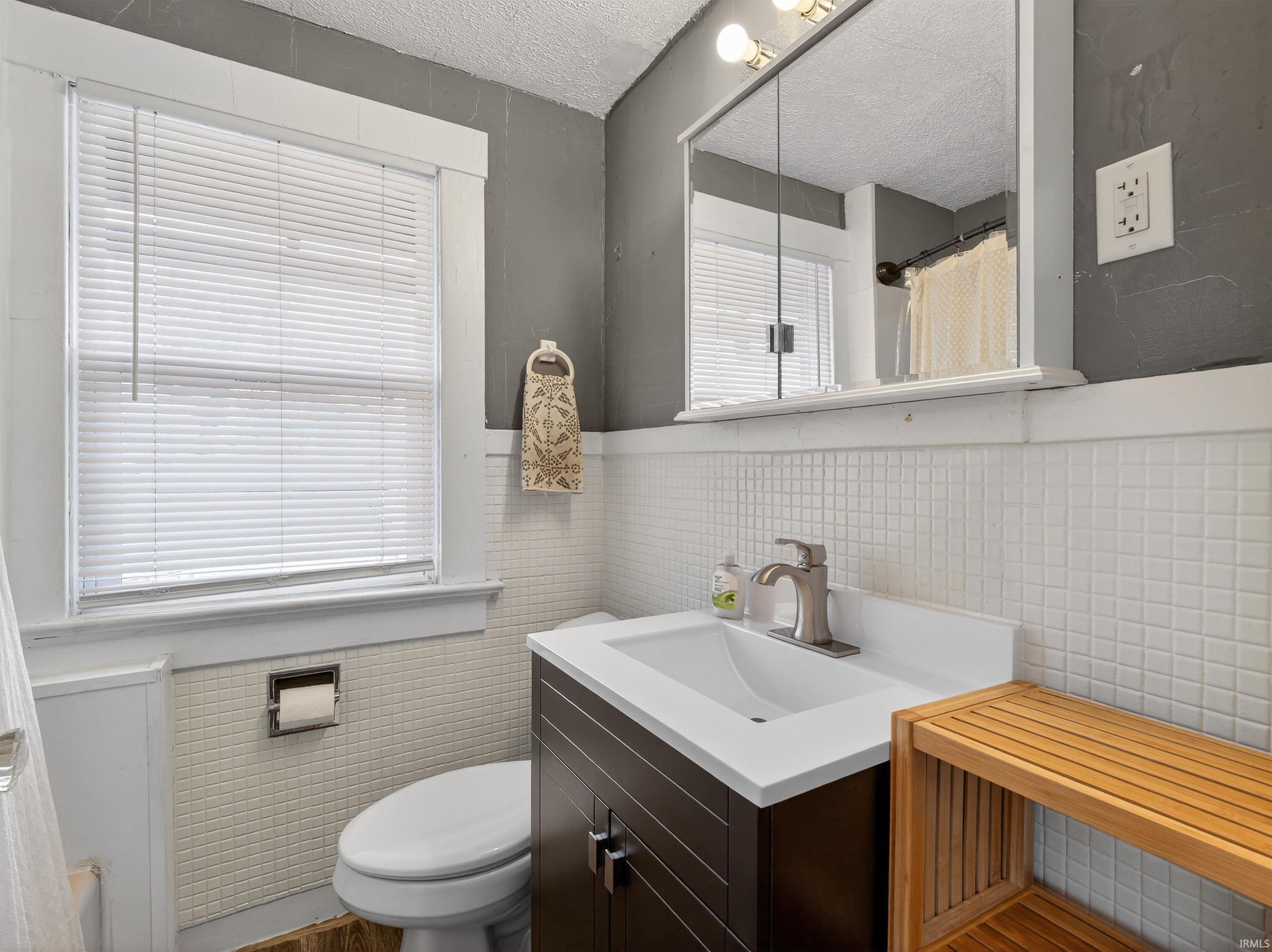 Bathroom featuring curtained shower, vanity, tile walls, a textured ceiling, and plenty of natural light