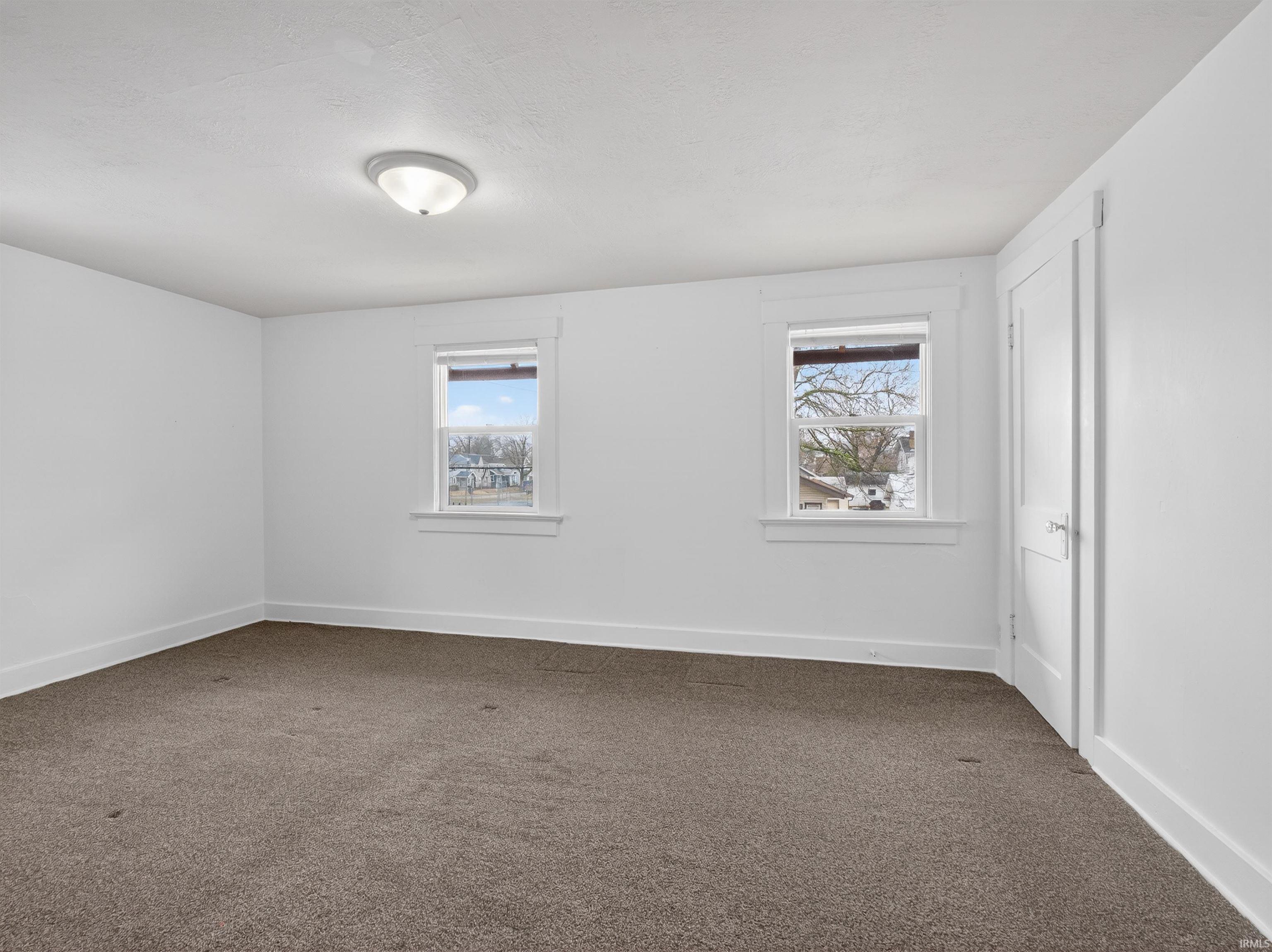 Spare room featuring dark colored carpet and baseboards