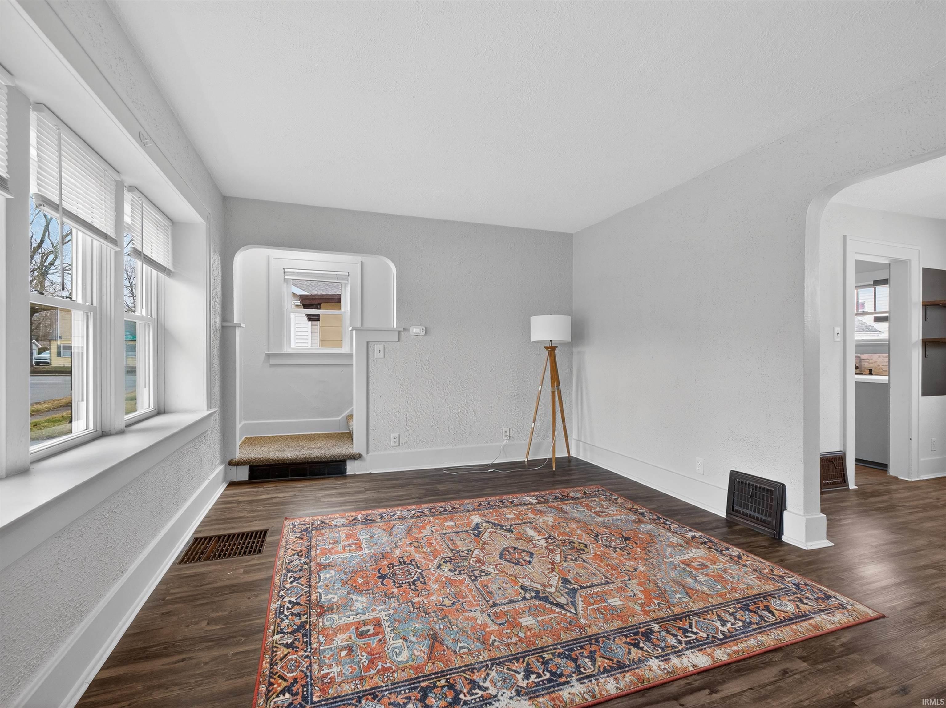 Unfurnished room featuring arched walkways, dark wood-style flooring, and a textured wall