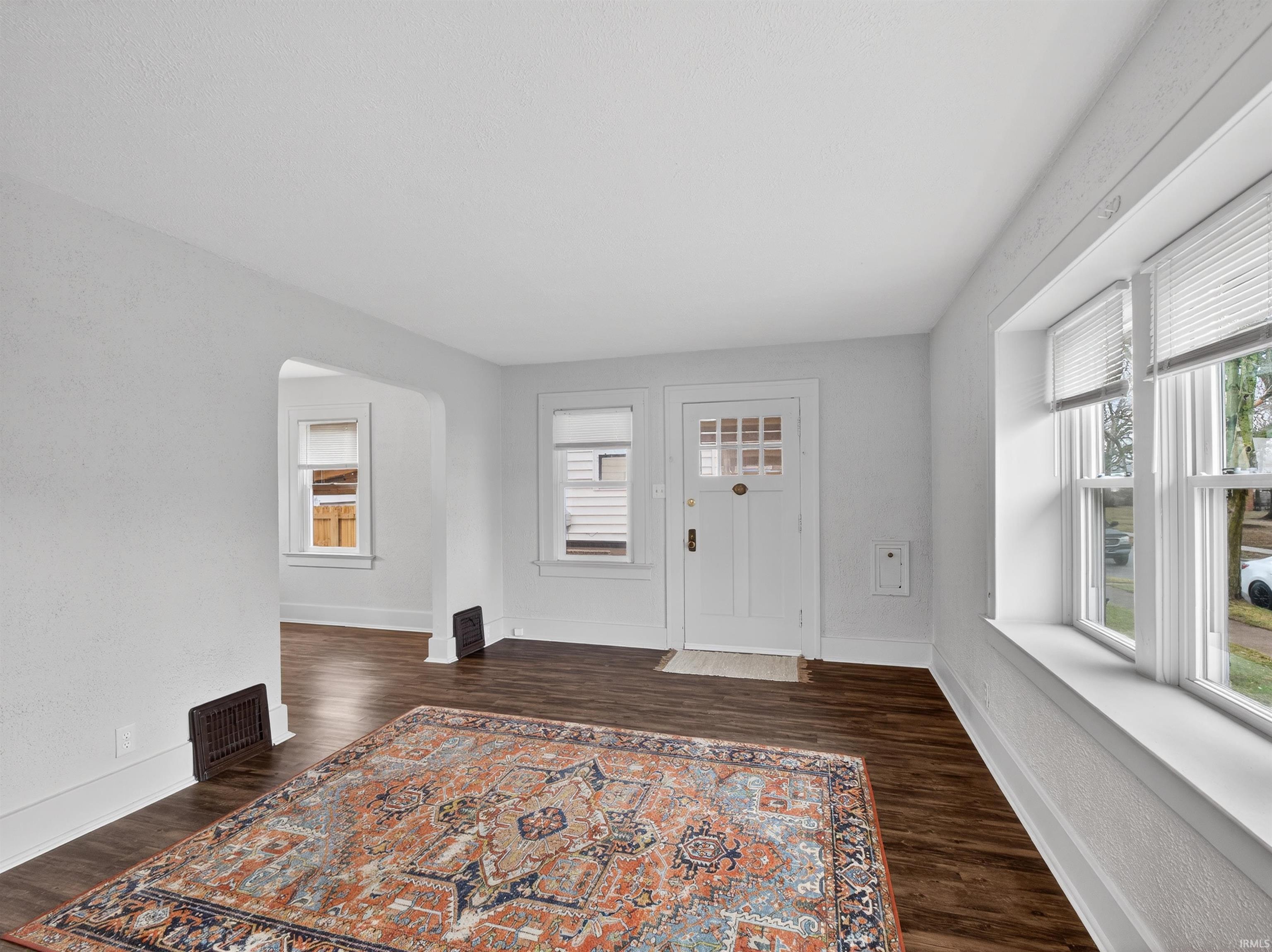 Entryway with arched walkways, dark wood finished floors, and a textured wall