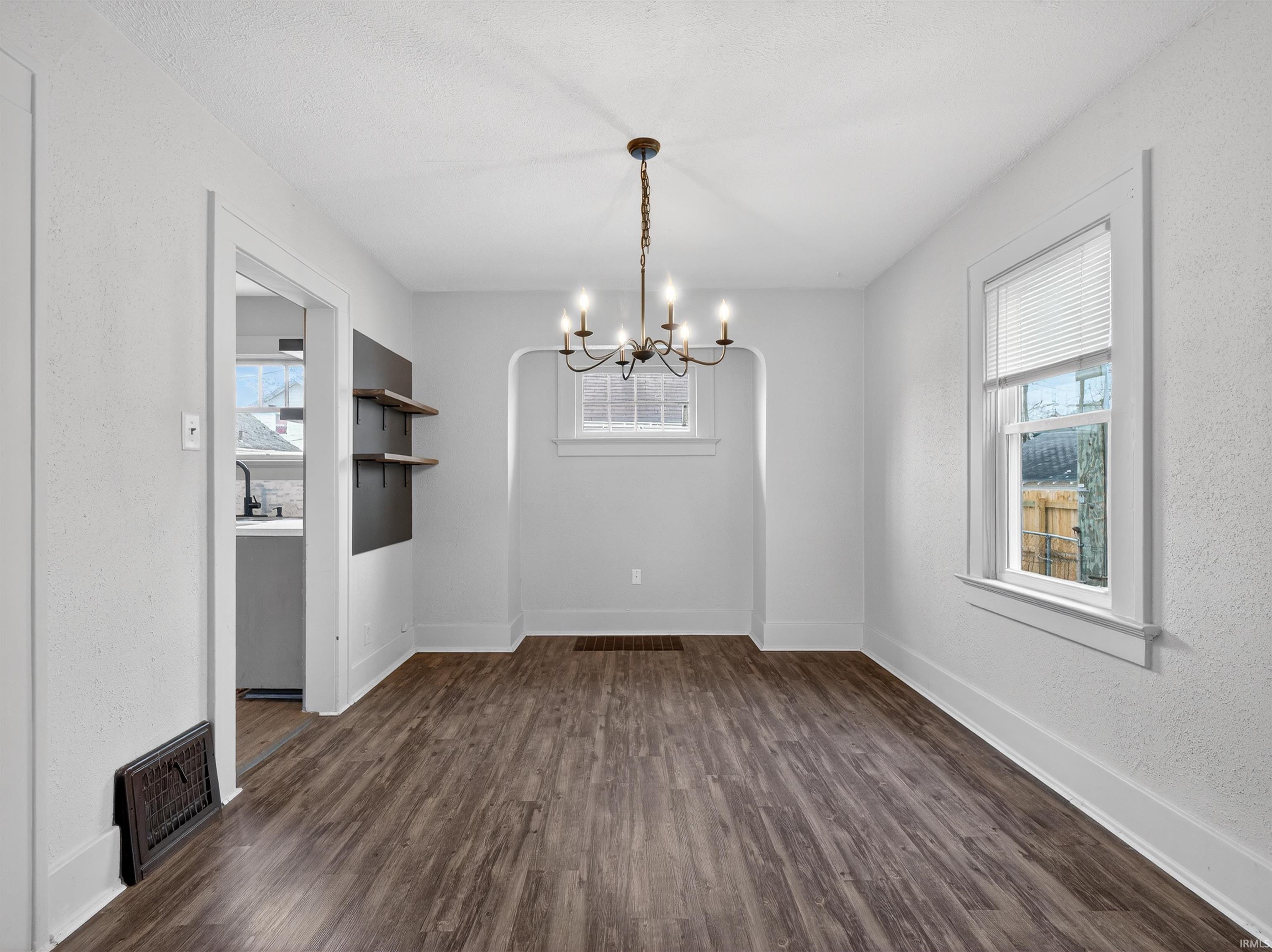 Unfurnished dining area with a chandelier, dark wood finished floors, and a textured wall