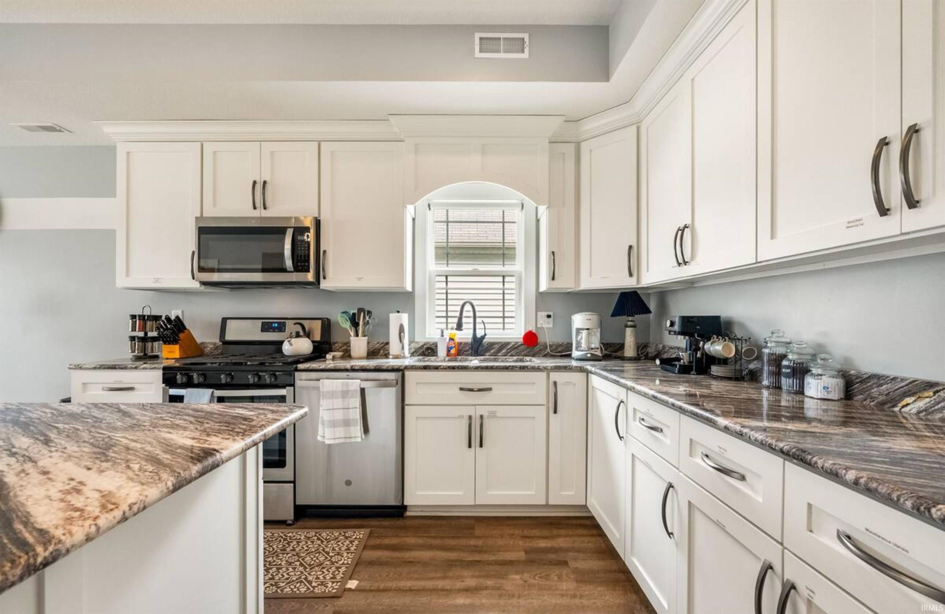 Kitchen featuring stainless steel appliances, dark stone countertops, white cabinetry, and dark wood-type flooring