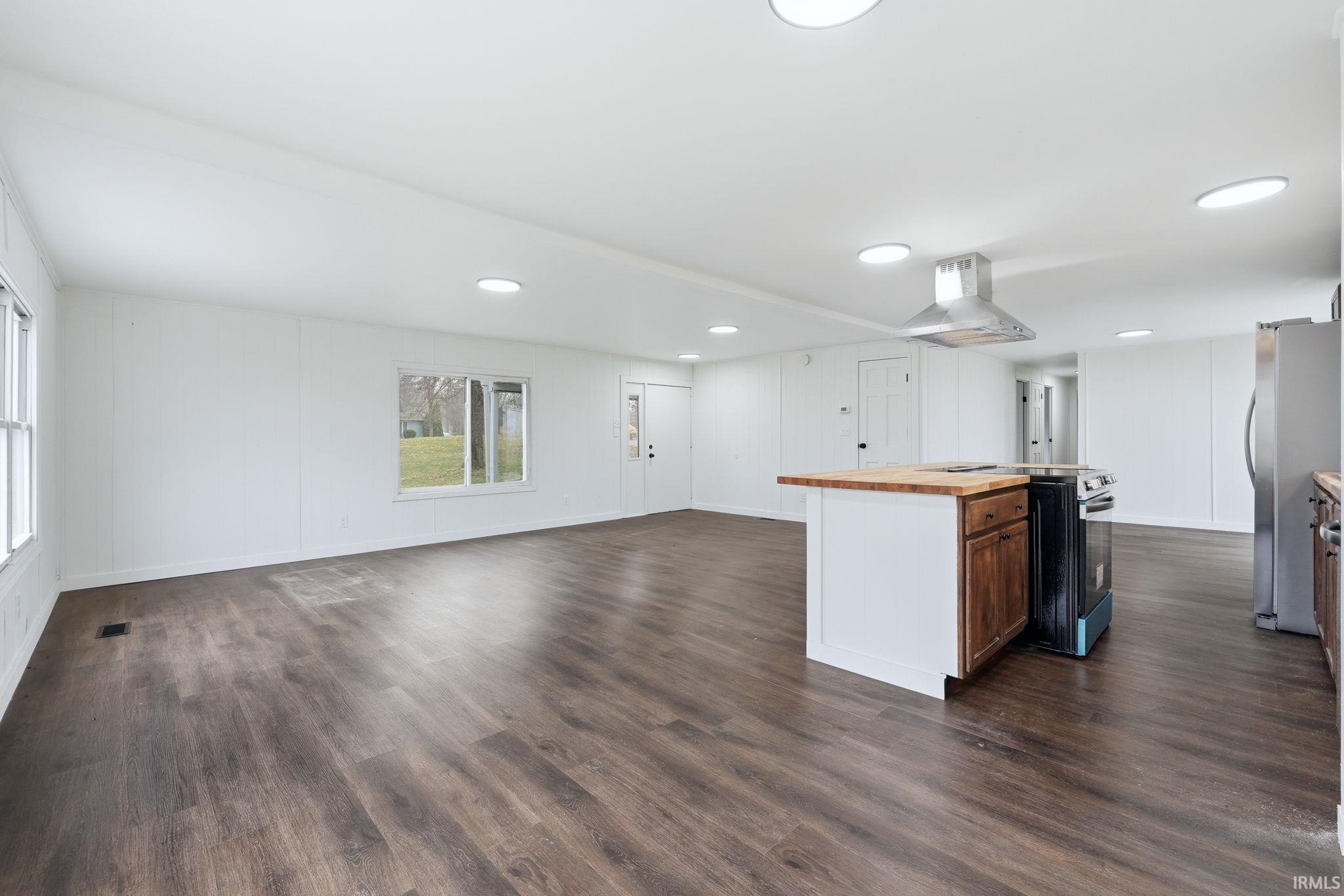 Kitchen with wood counters, open floor plan, stainless steel appliances, a kitchen island, and dark wood-style floors