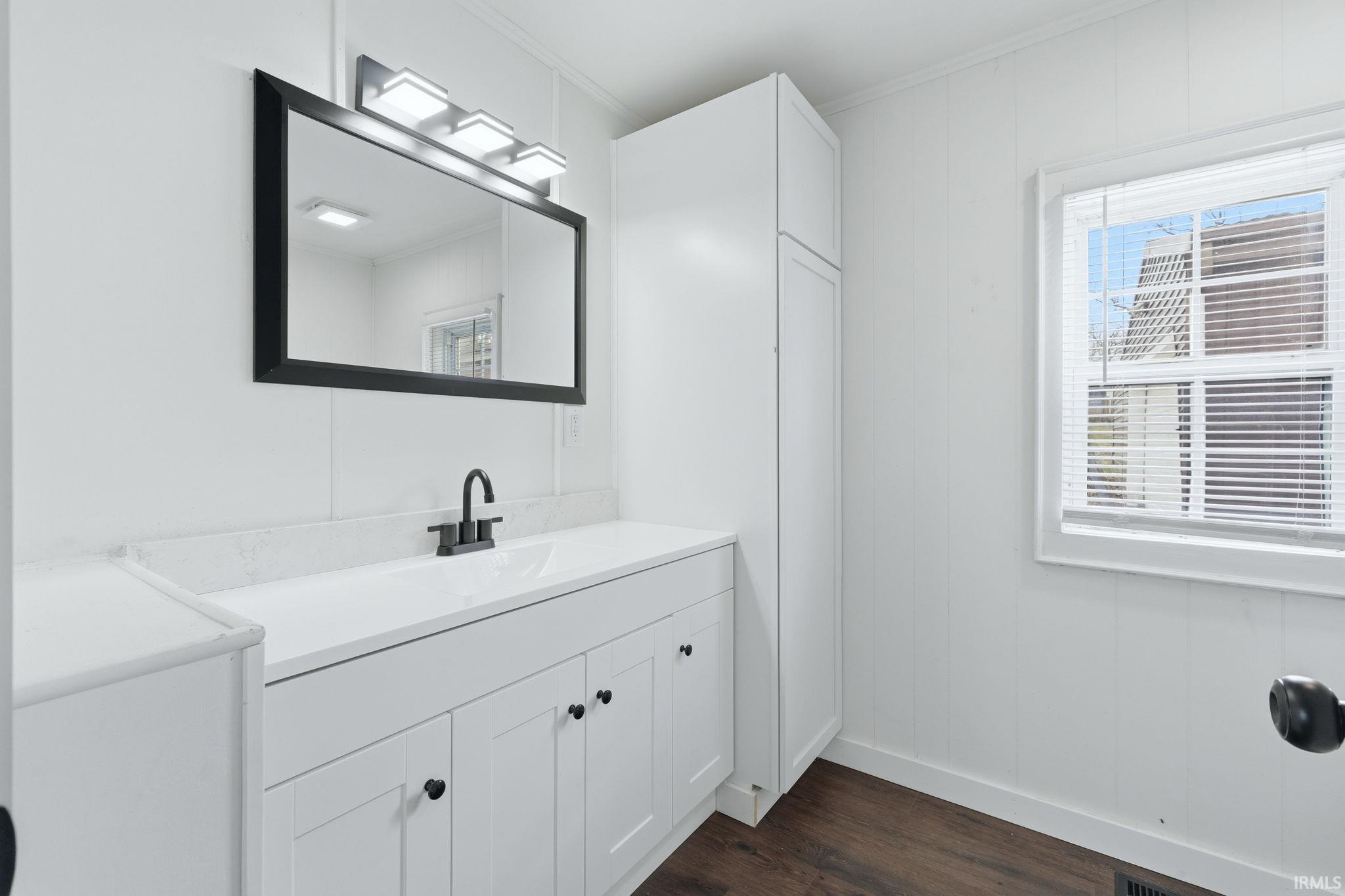 Bathroom featuring vanity, ornamental molding, and dark wood-style floors