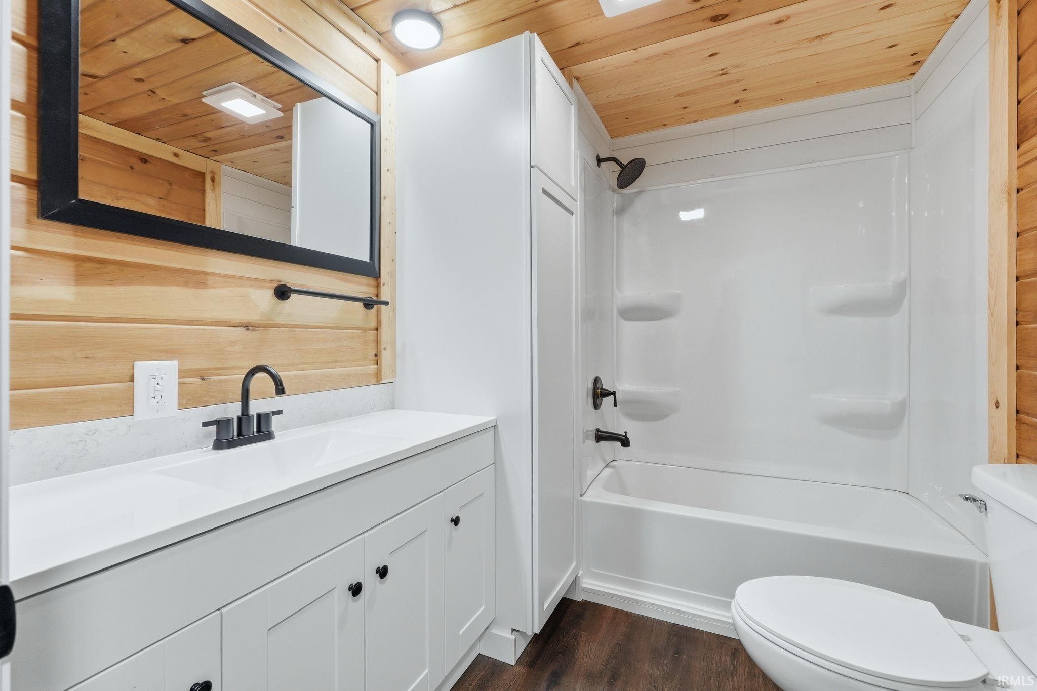Bathroom with wooden ceiling, wood walls, vanity, dark wood-style floors, and shower / bathtub combination