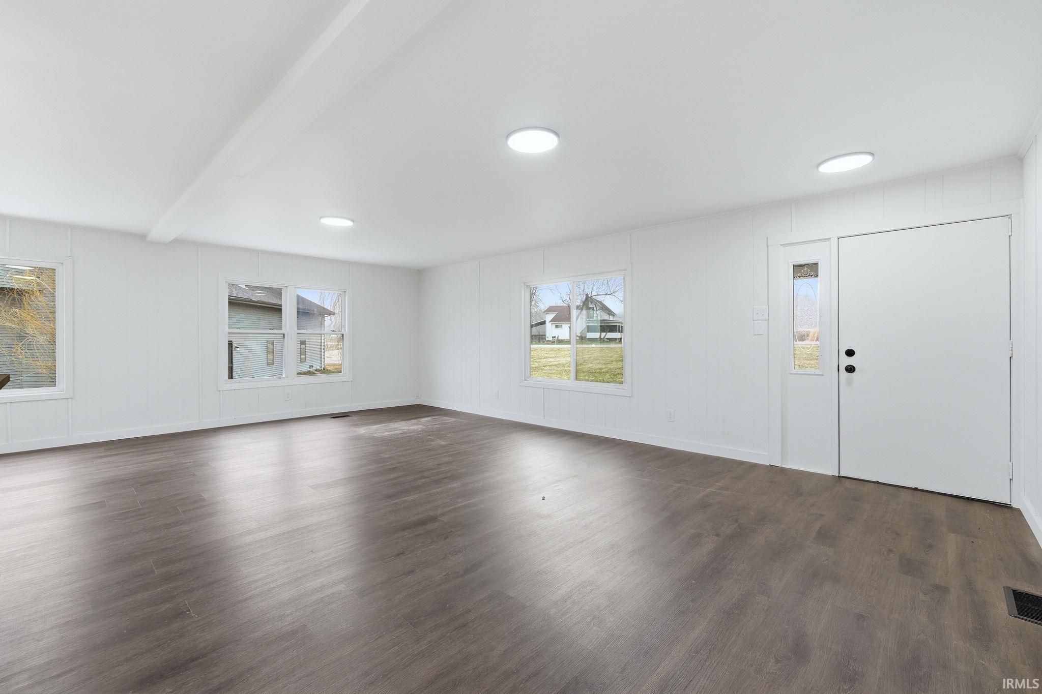 Unfurnished living room with beam ceiling, dark wood finished floors, and a decorative wall