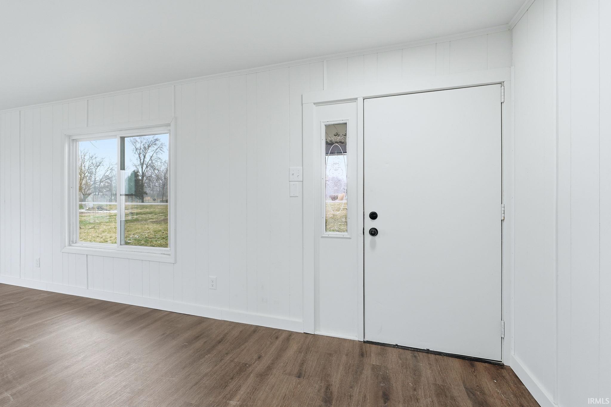 Entrance foyer with plenty of natural light, dark wood-style floors, ornamental molding, and wood walls