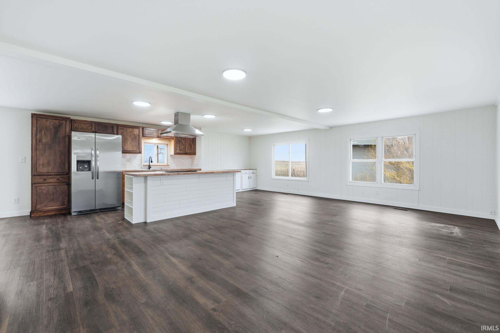 Dual tone kitchen with stainless steel refrigerator with ice dispenser, open floor plan, dark wood-style flooring, island range hood, and a kitchen island