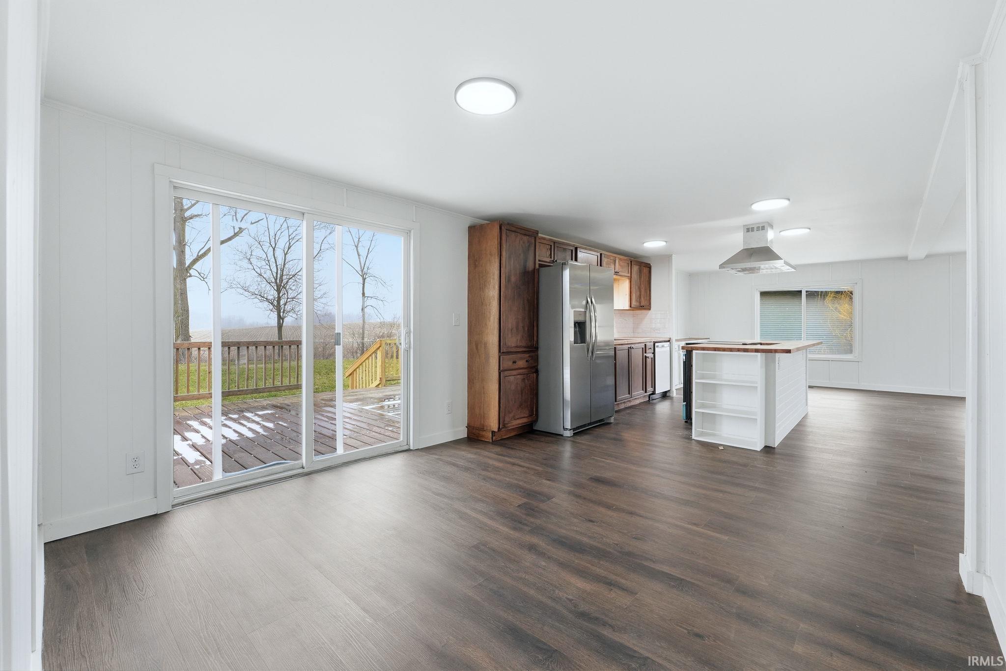 Kitchen with stainless steel refrigerator with ice dispenser, open shelves, dark wood-style flooring, a kitchen island, and exhaust hood