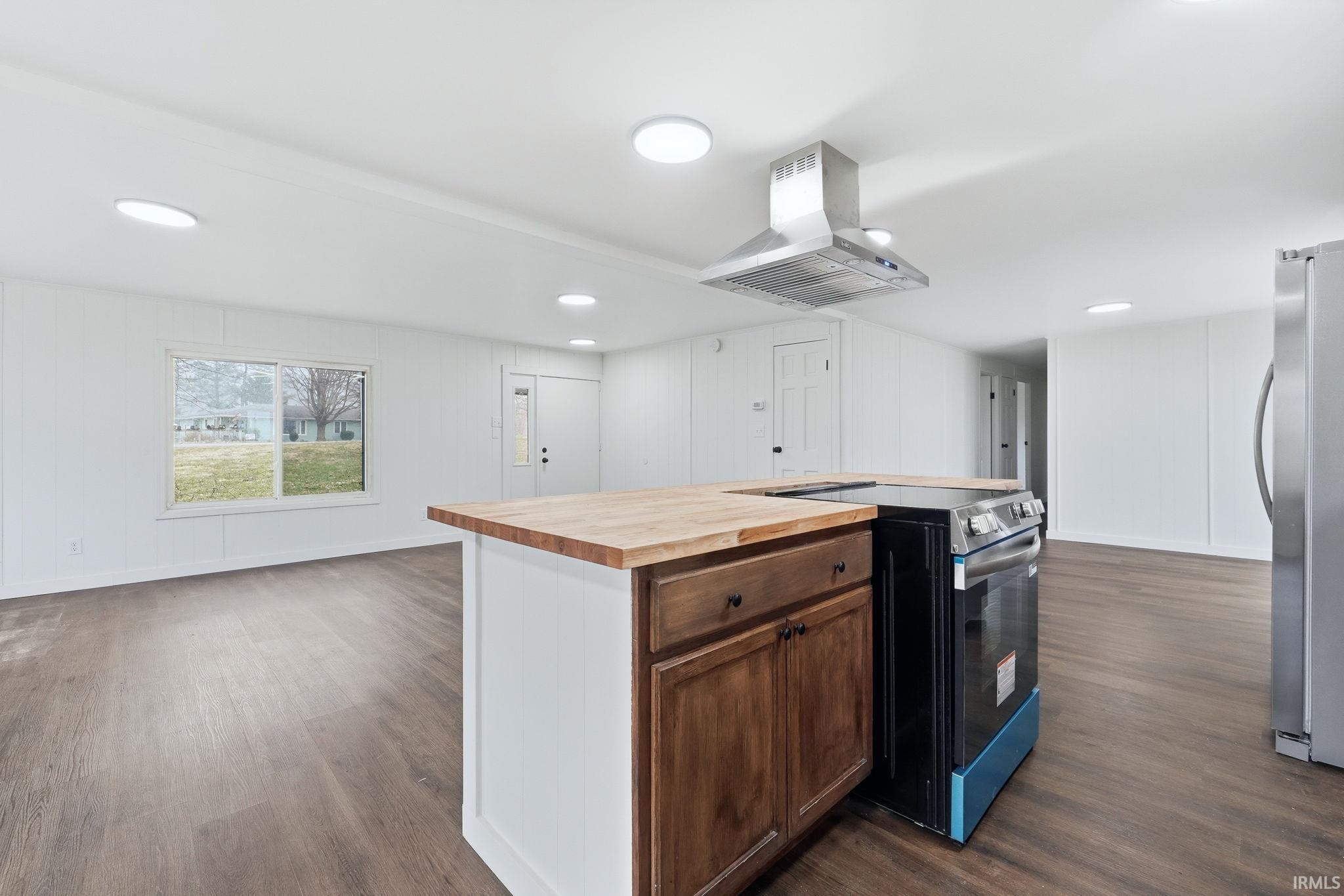 Kitchen featuring butcher block counters, stainless steel appliances, a kitchen island, island range hood, and dark wood-style floors