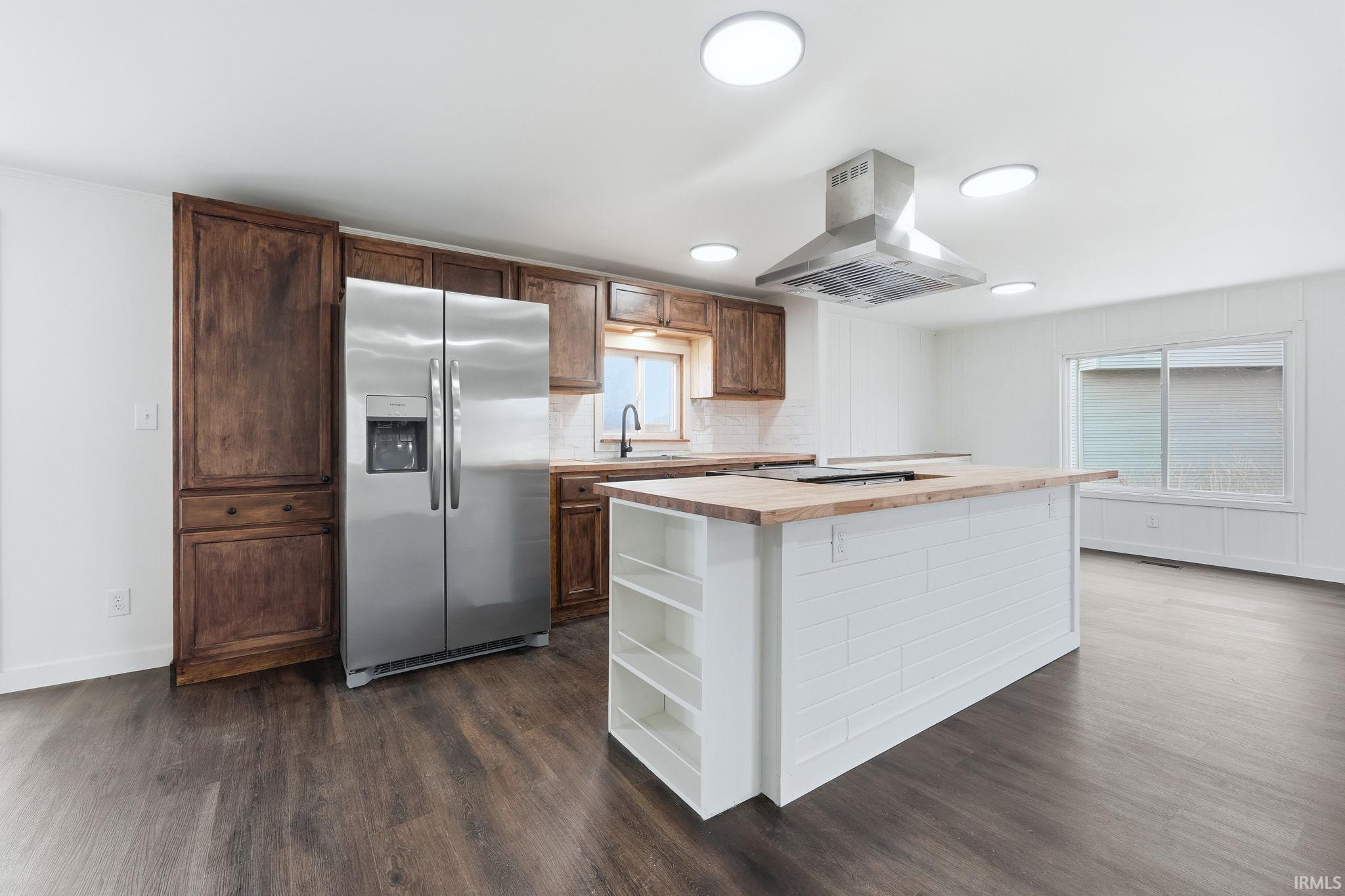 Two tone kitchen featuring stainless steel fridge, butcher block counters, a center island, island range hood, and dark wood-type flooring
