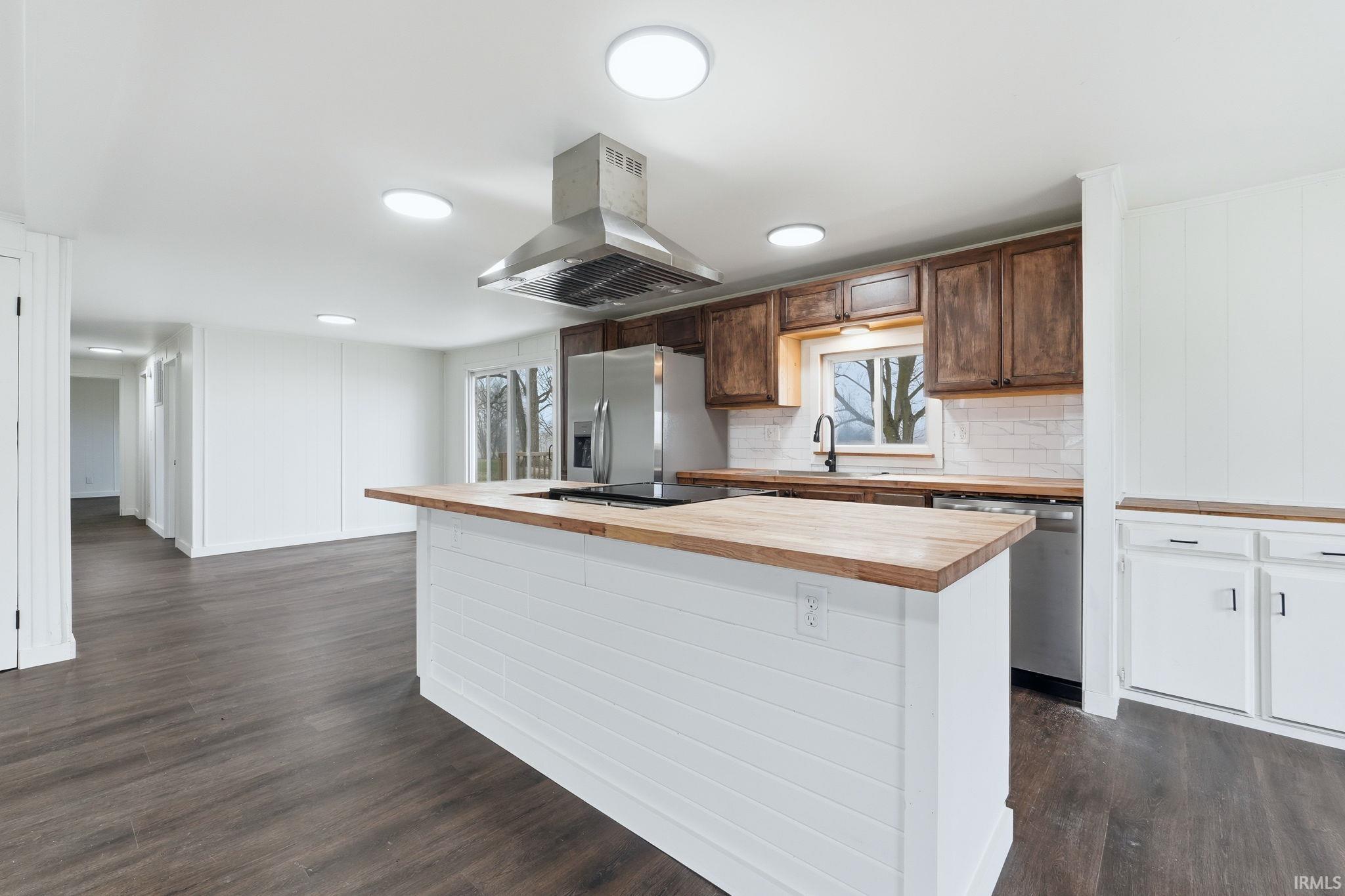 Kitchen with stainless steel appliances, island exhaust hood, butcher block counters, dark wood finished floors, and decorative backsplash
