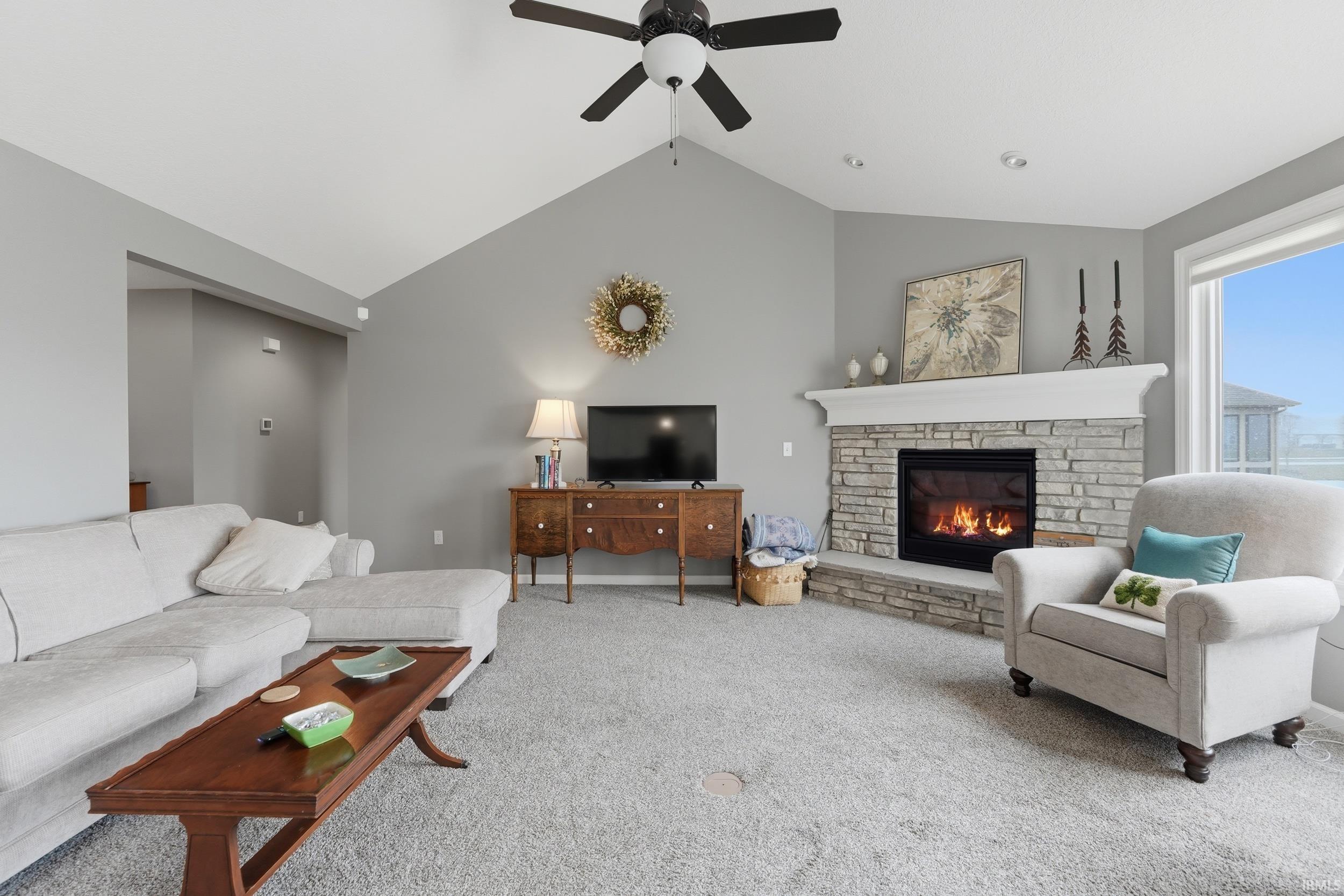 Living area with carpet flooring, a fireplace, ceiling fan, and a high ceiling
