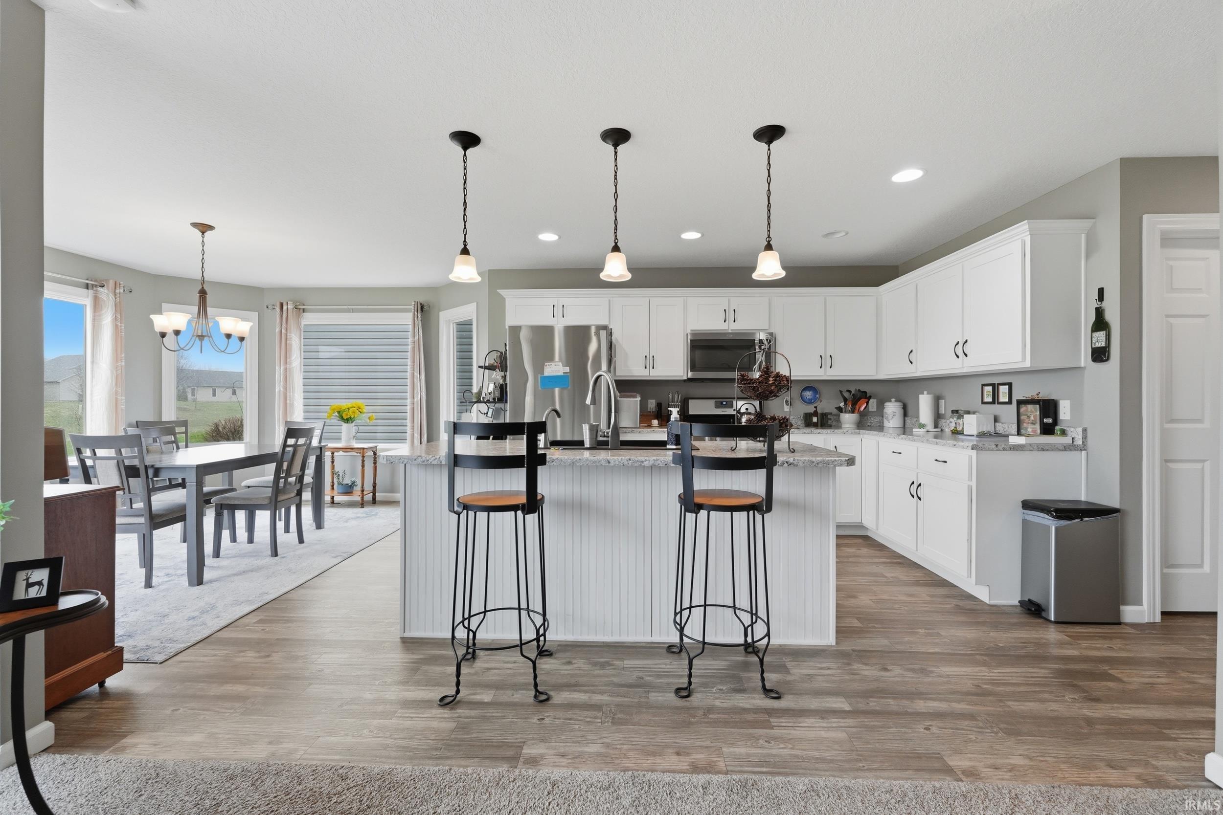 Kitchen with light wood-style flooring, white cabinetry, a center island with sink, and hanging lights