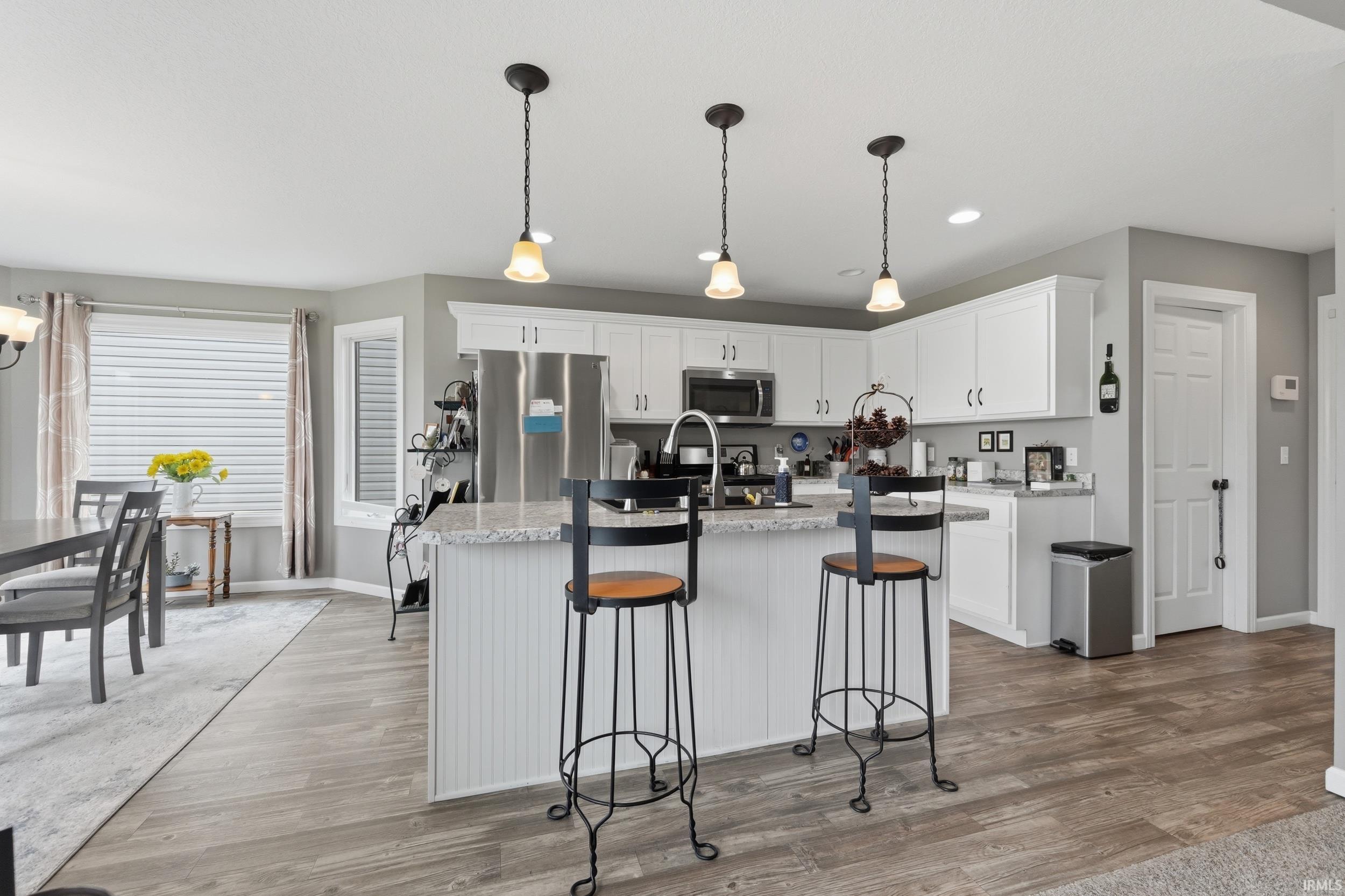 Kitchen with decorative light fixtures, white cabinets, a kitchen island with sink, stainless steel appliances, and light stone countertops