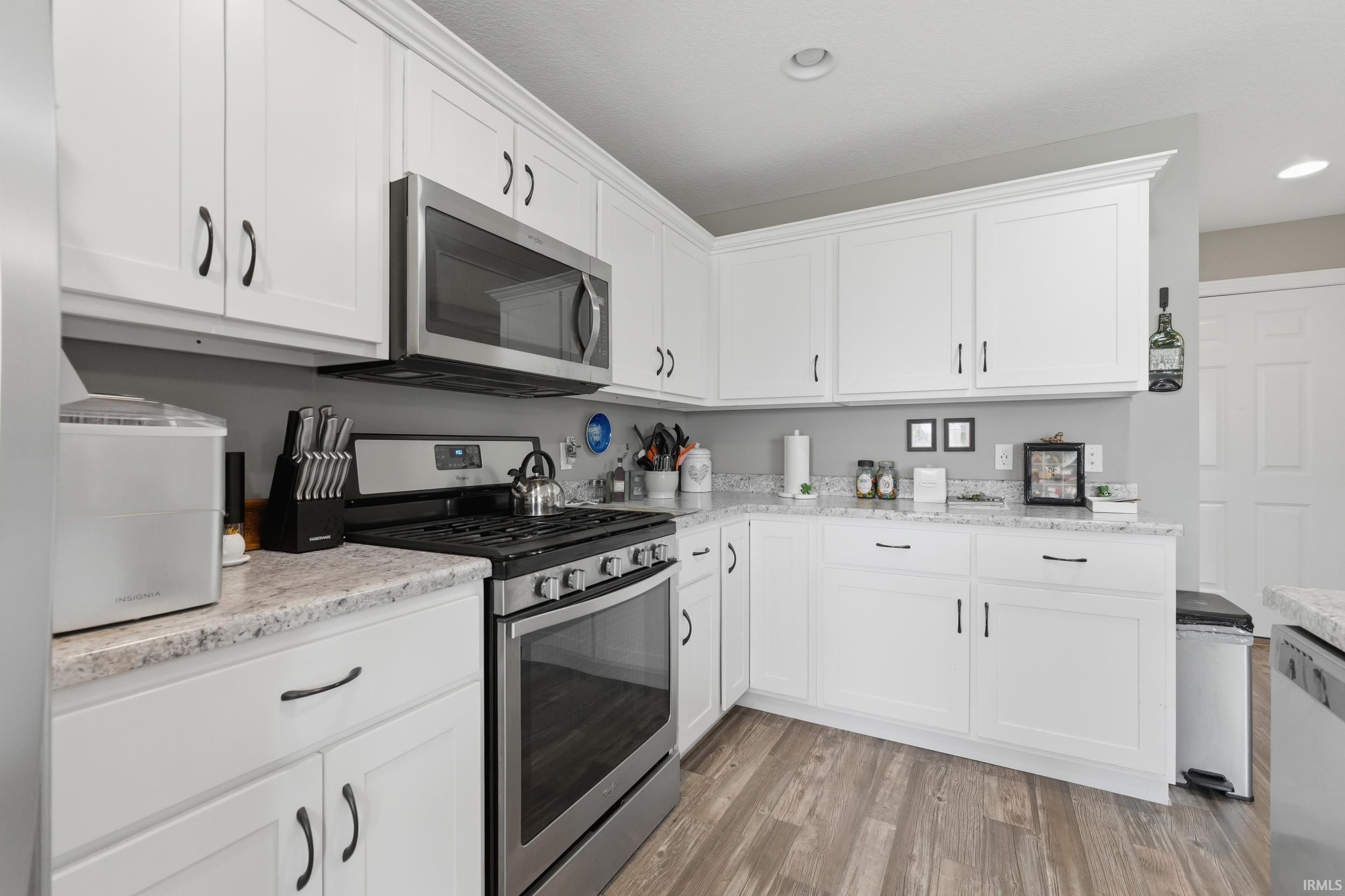 Kitchen with stainless steel appliances, white cabinets, light wood-style floors, light stone countertops, and recessed lighting