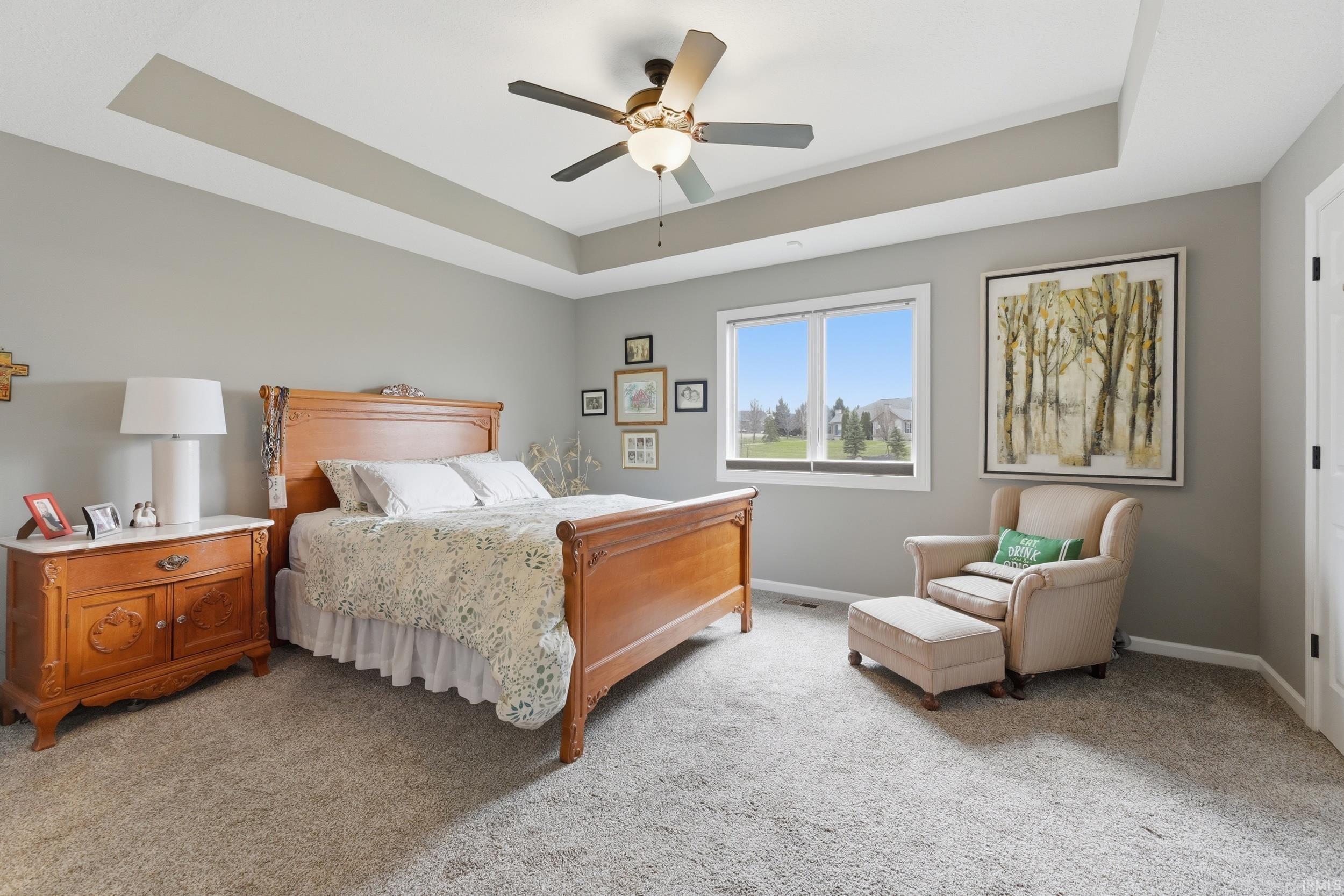 Bedroom with a tray ceiling, light colored carpet, and ceiling fan