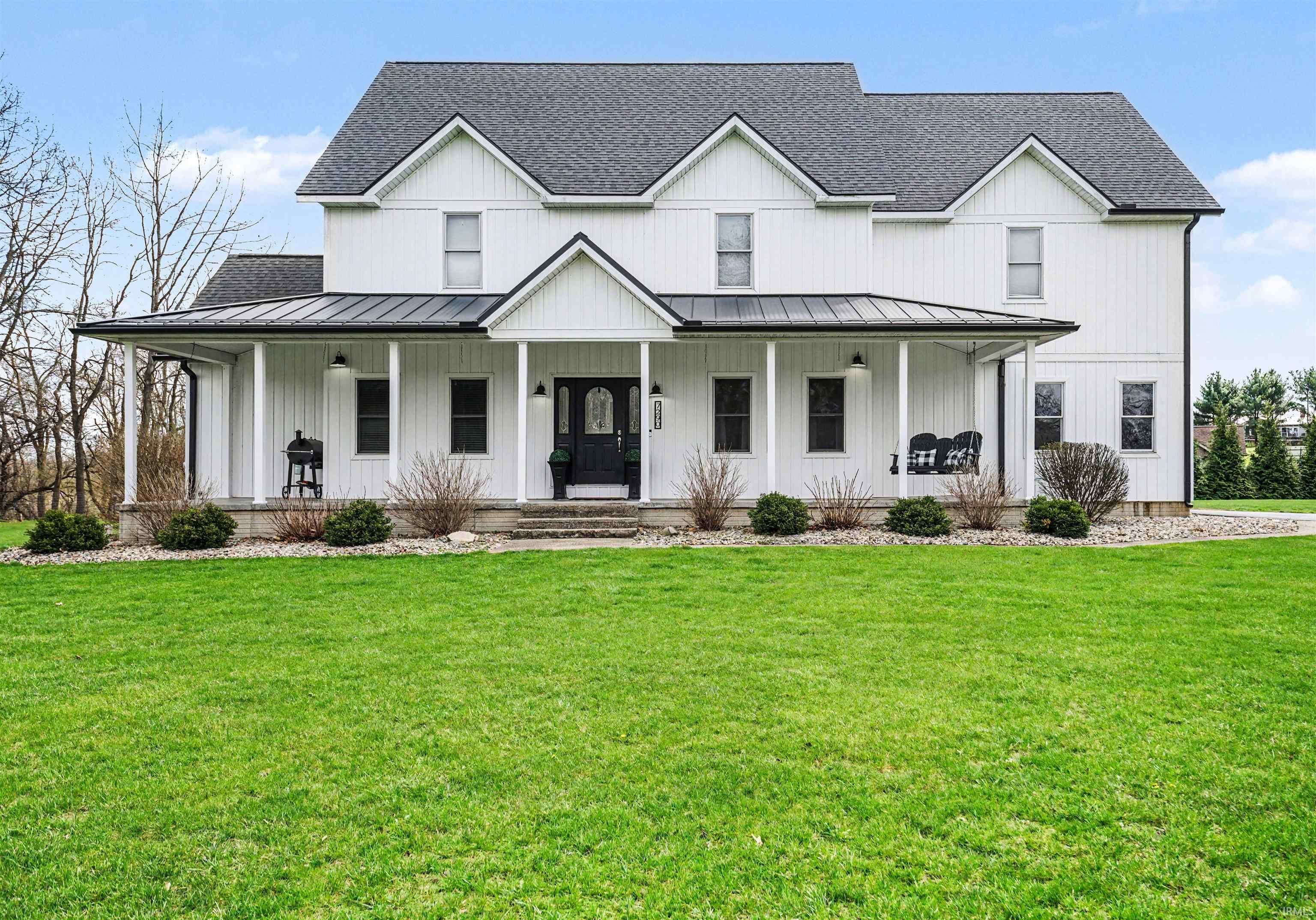Modern farmhouse style home featuring roof with shingles, covered porch, a front yard, a standing seam roof, and board and batten siding