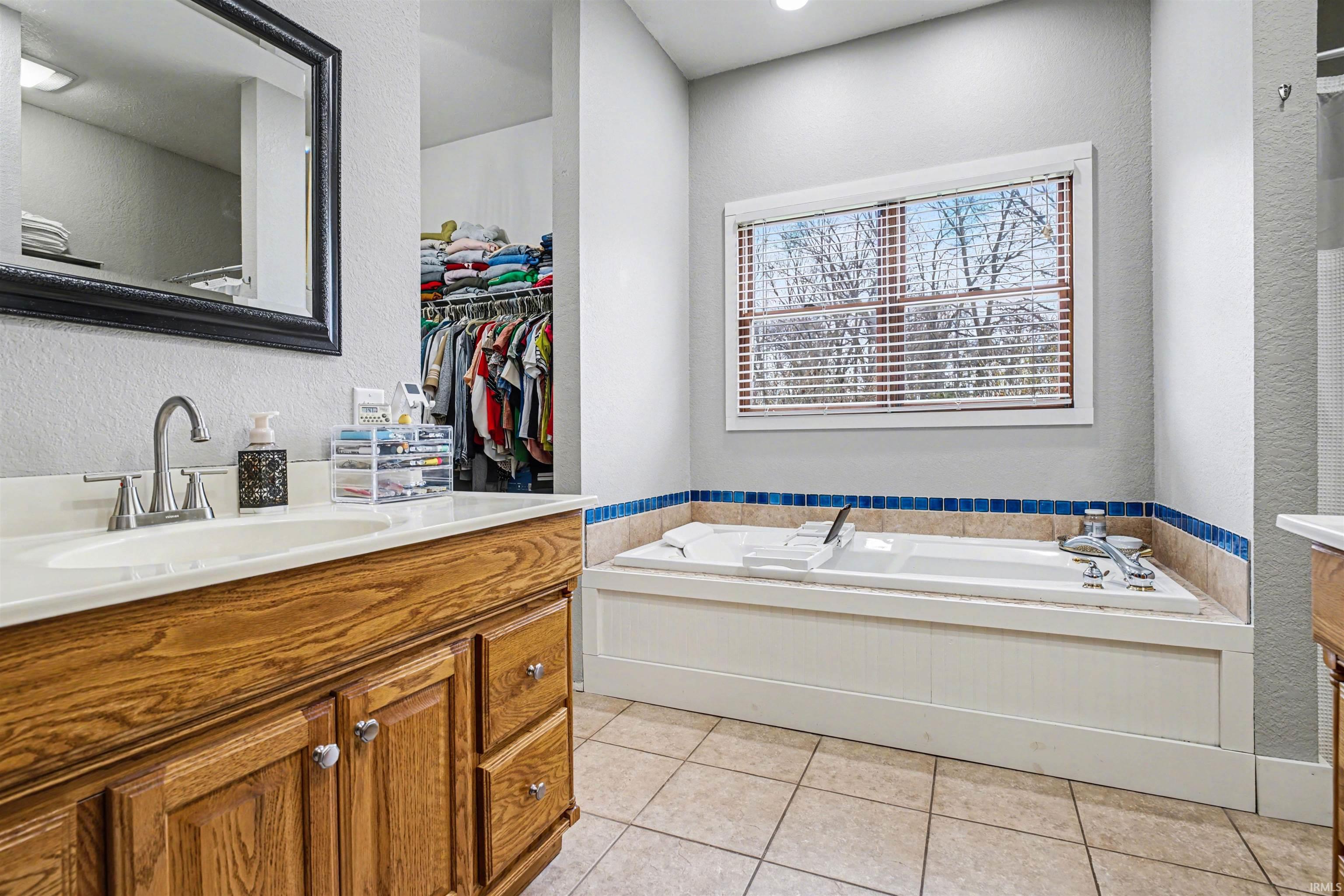 Bathroom featuring vanity, a textured wall, a bath, and light tile patterned floors