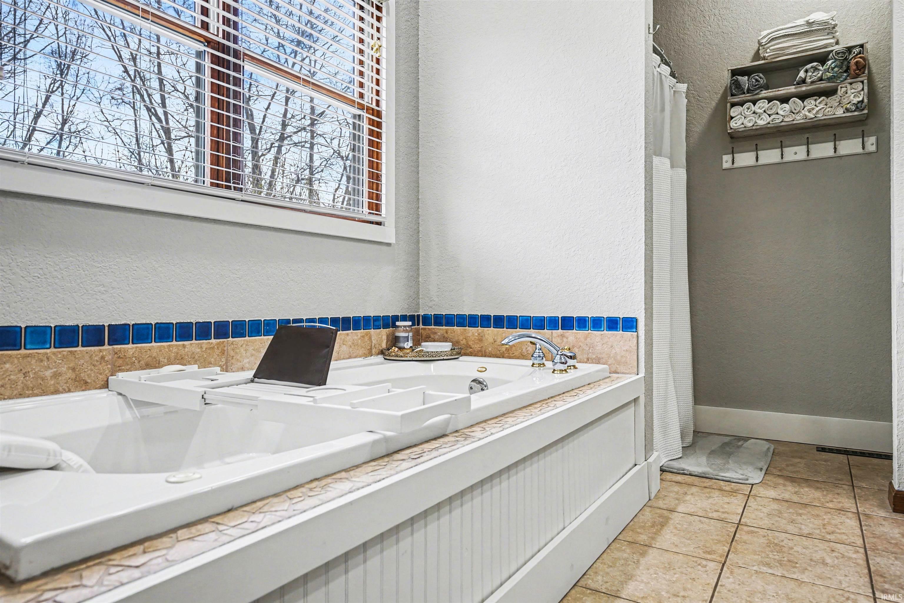 Full bath with a textured wall, a bath, a shower with curtain, and light tile patterned flooring