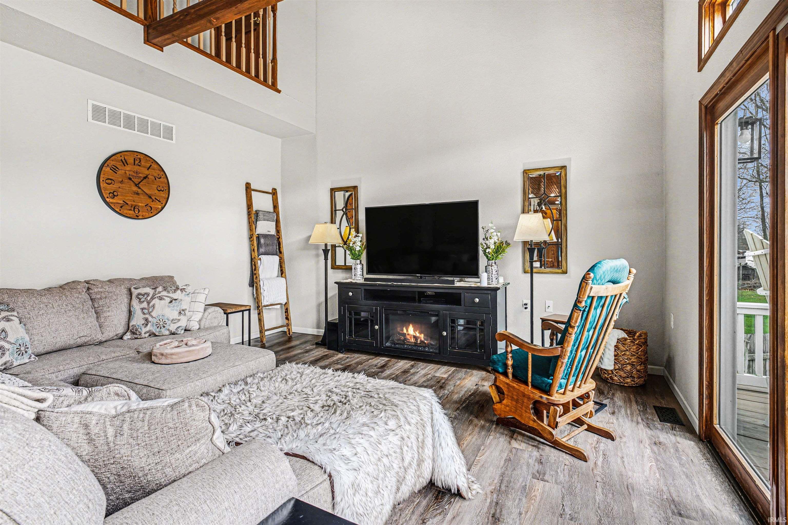 Living room featuring wood finished floors, a high ceiling, a glass covered fireplace, and plenty of natural light