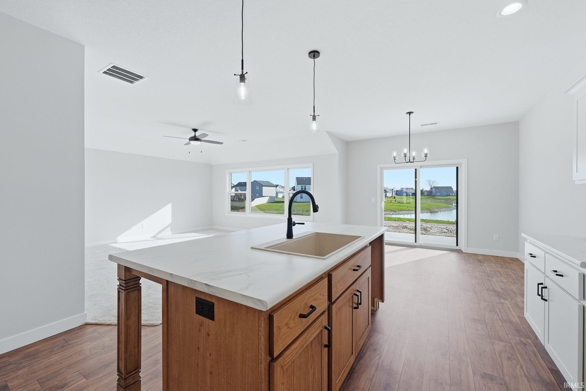 Kitchen featuring dark wood-style flooring, a kitchen island with sink, wood finish cabinets, and hanging lights