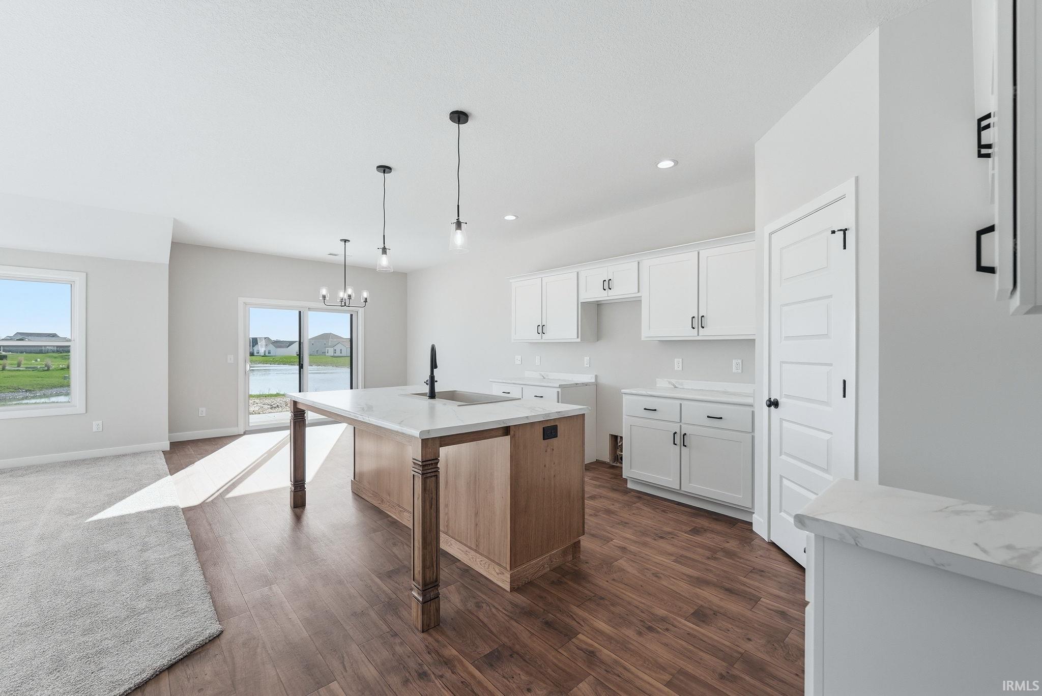 Kitchen featuring a breakfast bar area, a kitchen island with sink, hanging lights, dark wood-style flooring, and two tone color scheme
