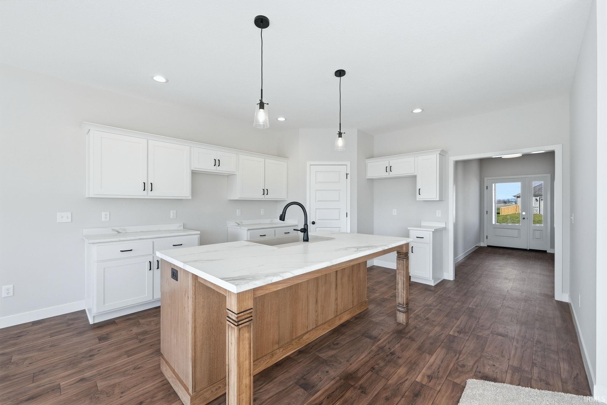 Dual tone kitchen featuring an island with sink, dual tone cabinets, dark wood finished floors, pendant lighting, and light stone countertops