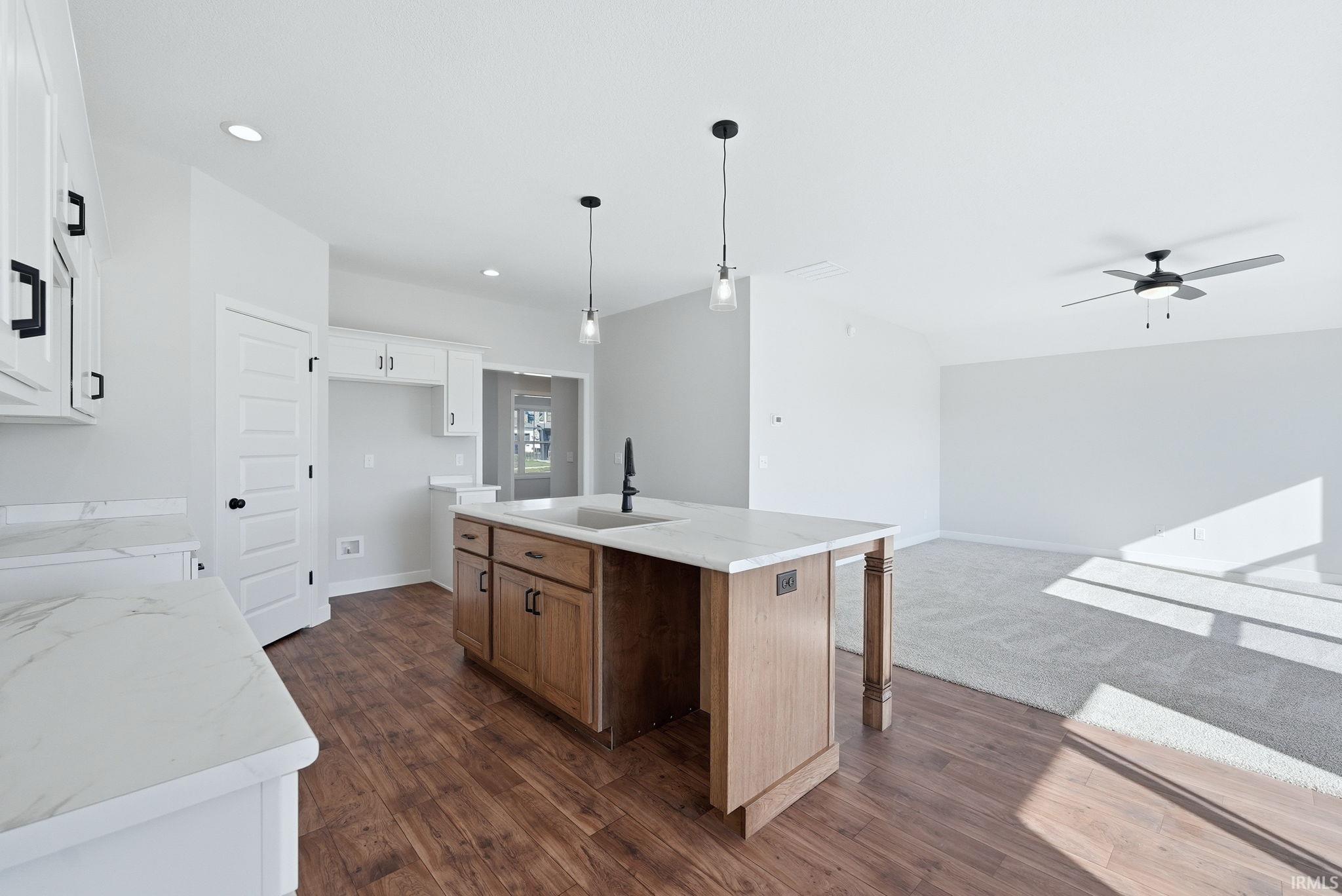 Two tone kitchen featuring an island with sink, two tone cabinets, light stone counters, open floor plan, and a ceiling fan