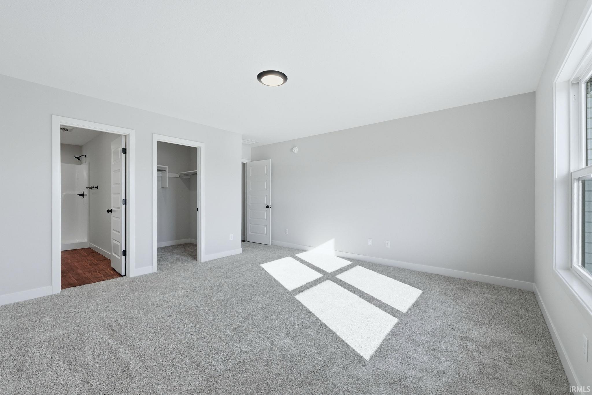 Unfurnished bedroom with a walk in closet, light carpet, and connected bathroom