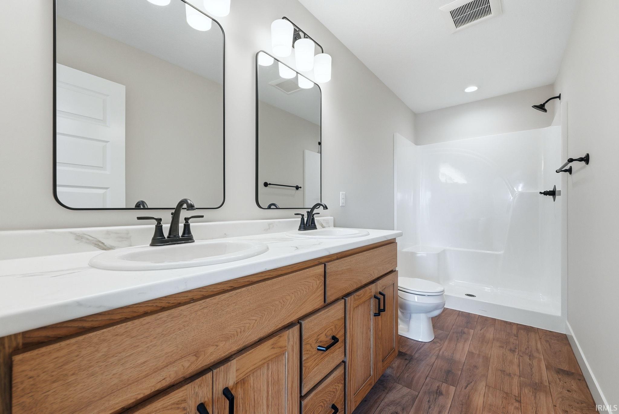 Full bathroom featuring double vanity, a shower stall, dark wood-style floors, and recessed lighting