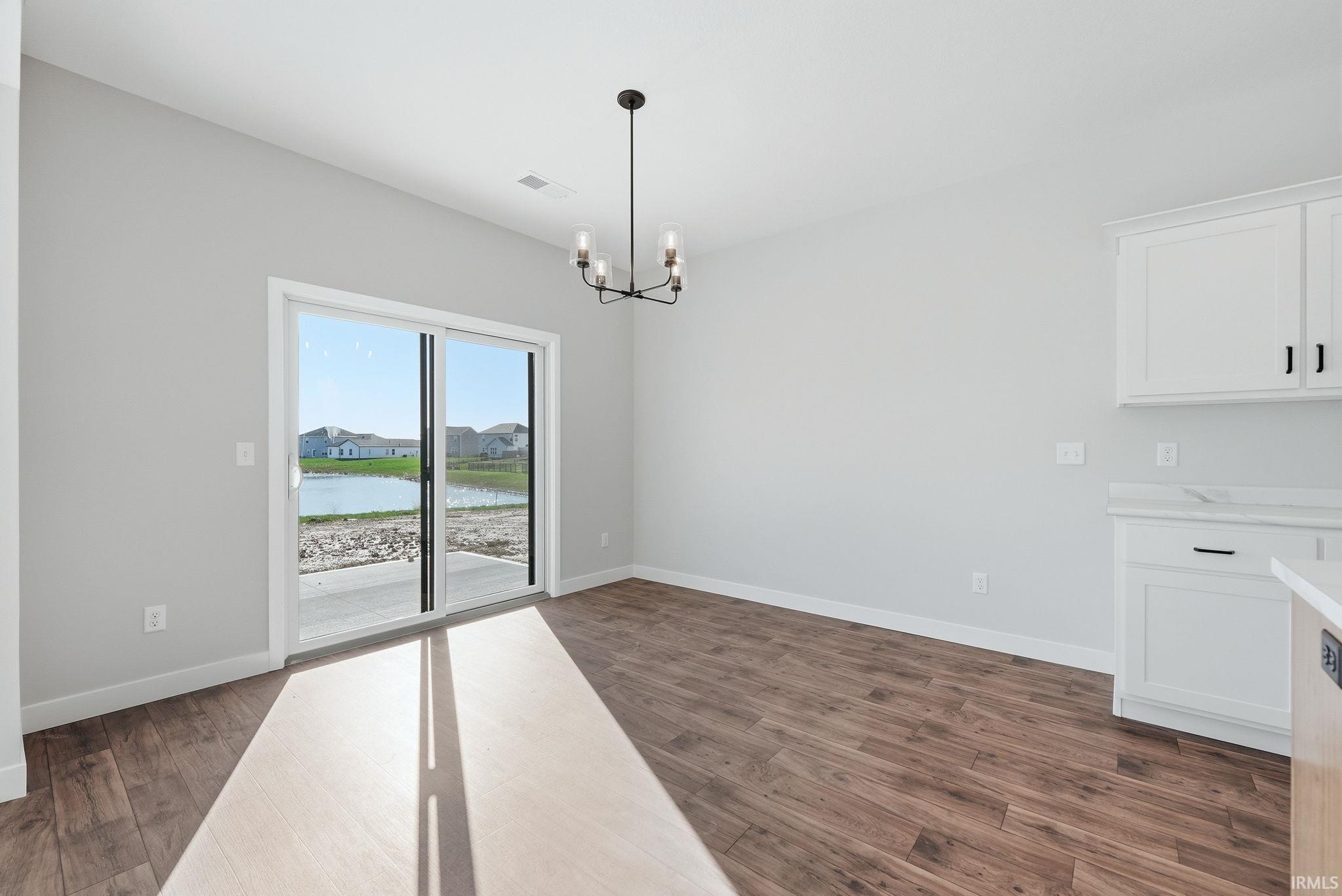 Unfurnished dining area with a chandelier, dark wood-style flooring, and a water view