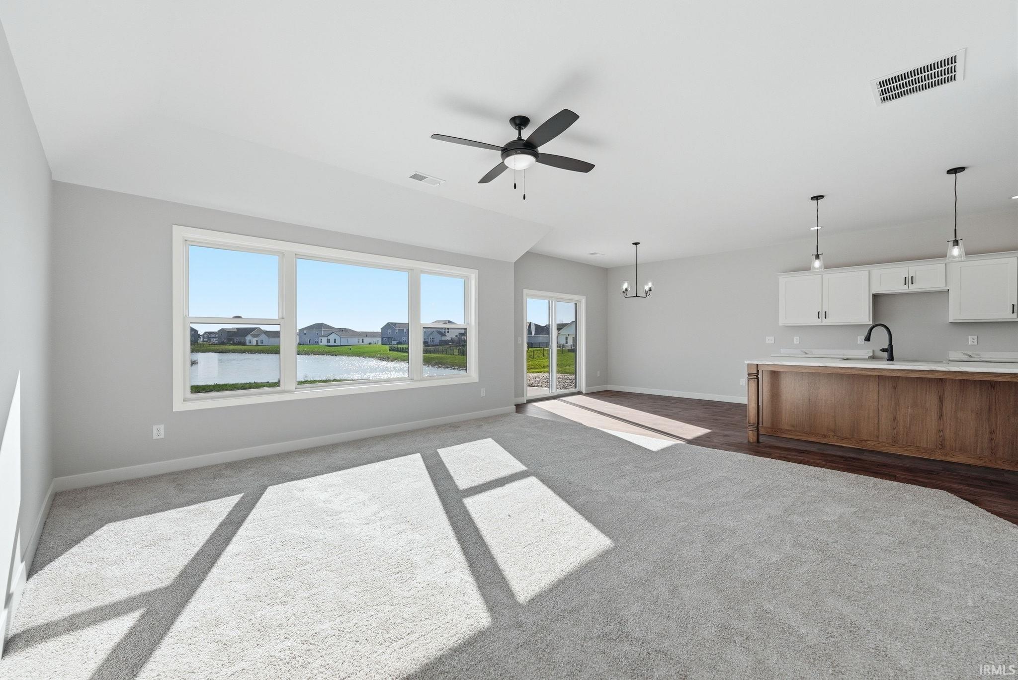 Unfurnished living room with a chandelier, dark carpet, ceiling fan, and a water view