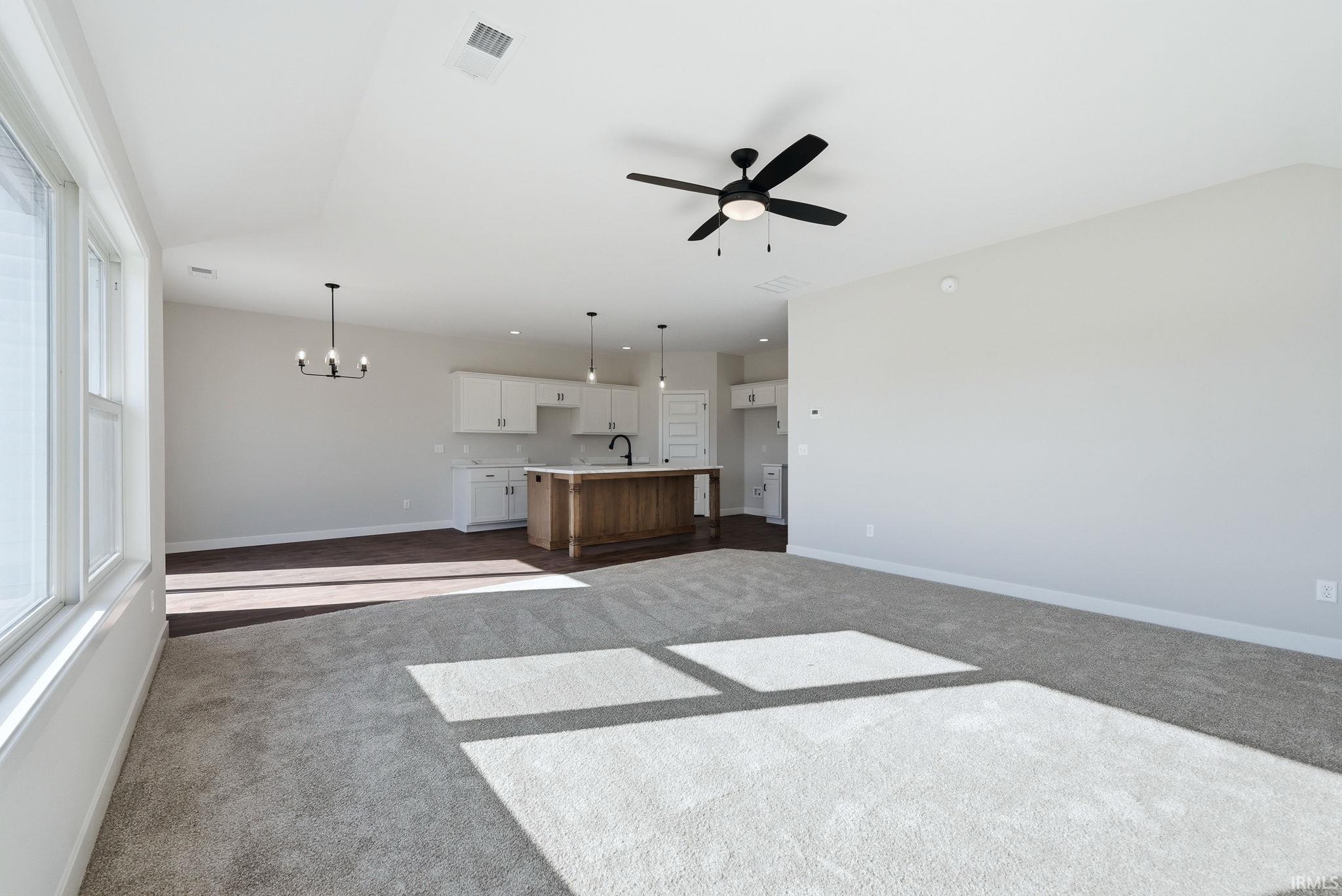 Unfurnished living room with ceiling fan, hanging lights, and dark carpet