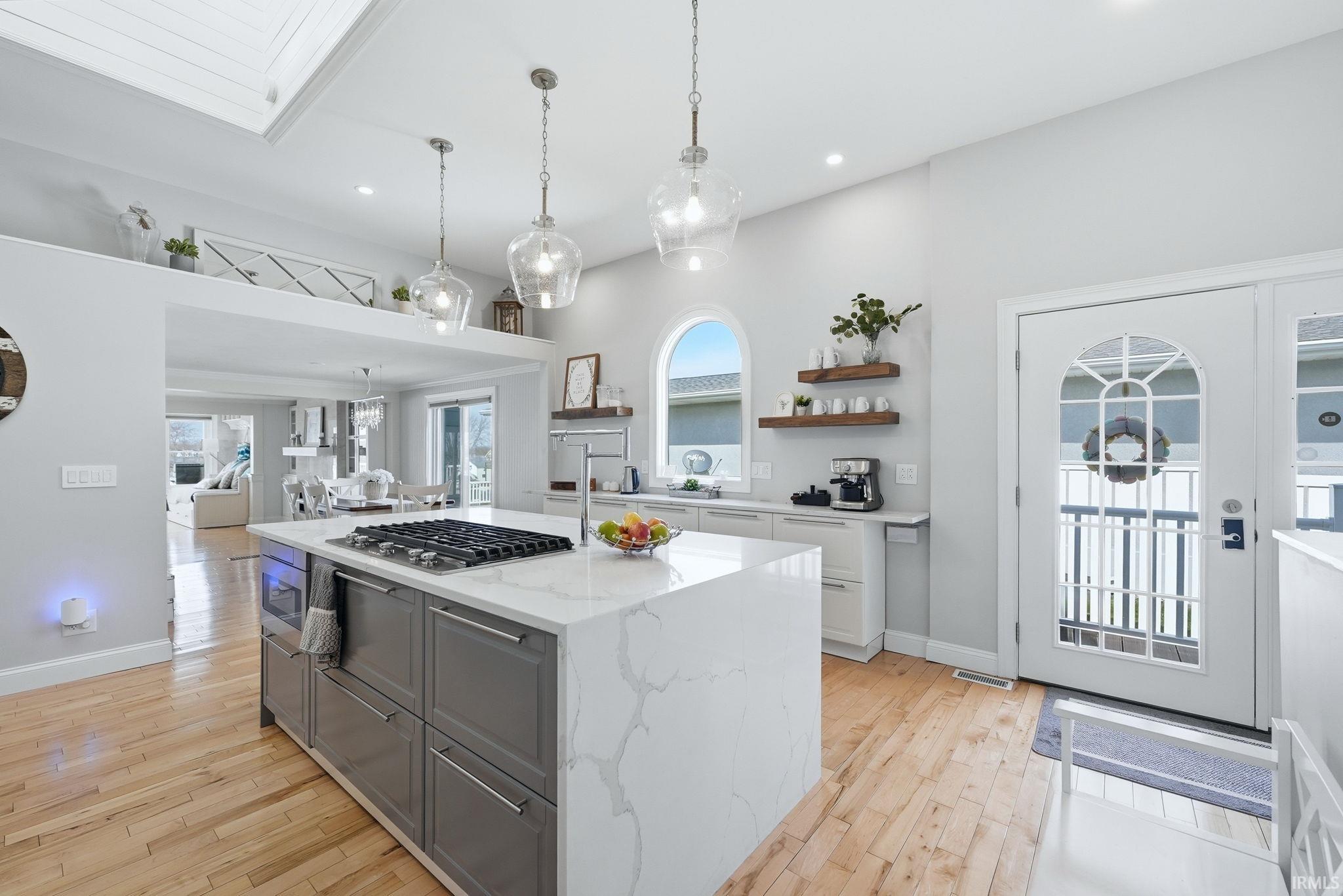 Kitchen with light stone counters, gray cabinets, a kitchen island with sink, light wood-style floors, and open shelves