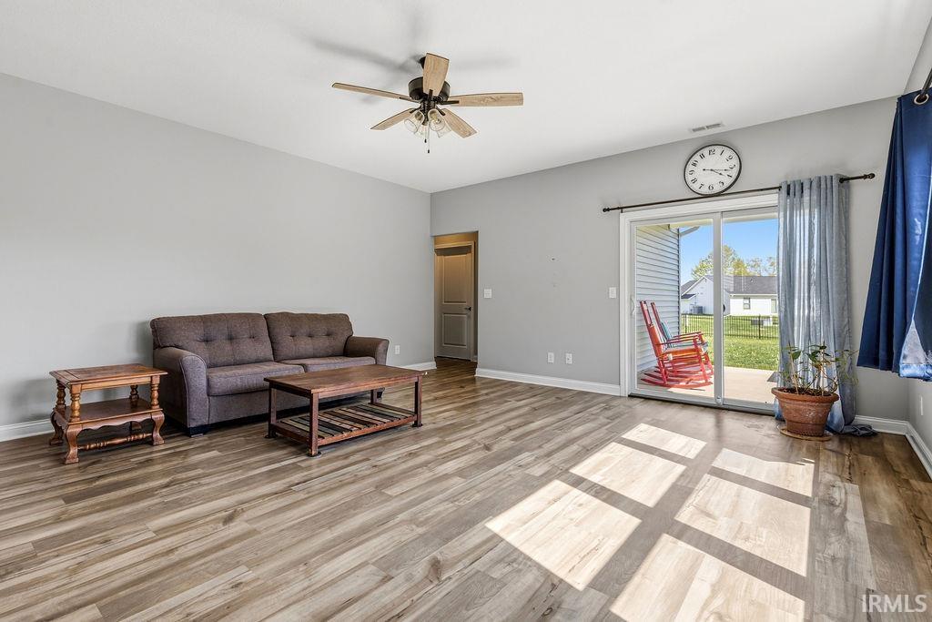 Spacious living area featuring wood-finish flooring, a ceiling fan with integrated lighting, and light gray walls