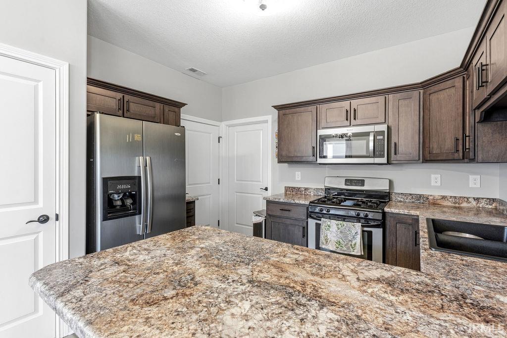 Kitchen featuring dark wood-finish cabinetry, stainless steel appliances, and multi-toned countertops