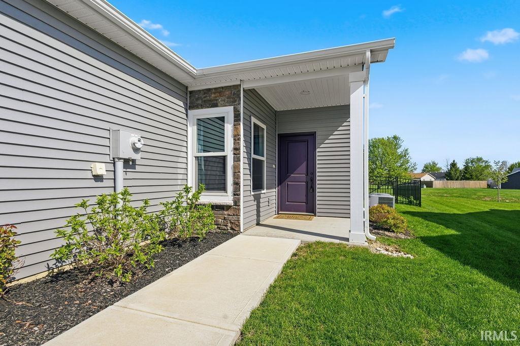Inviting entryway featuring a covered porch, purple front door, gray horizontal siding, and stone veneer accents