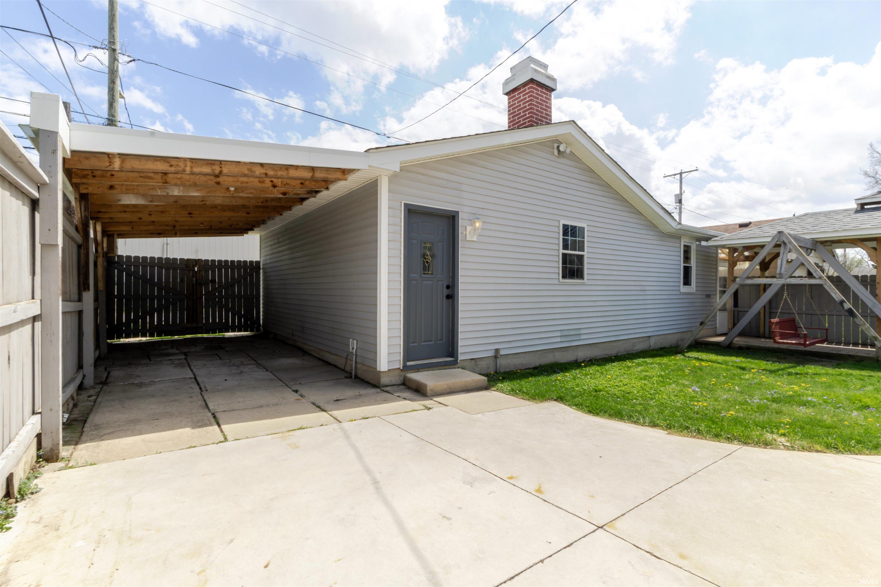 View of side of property with a patio area, driveway, an attached carport, a chimney, and a gate
